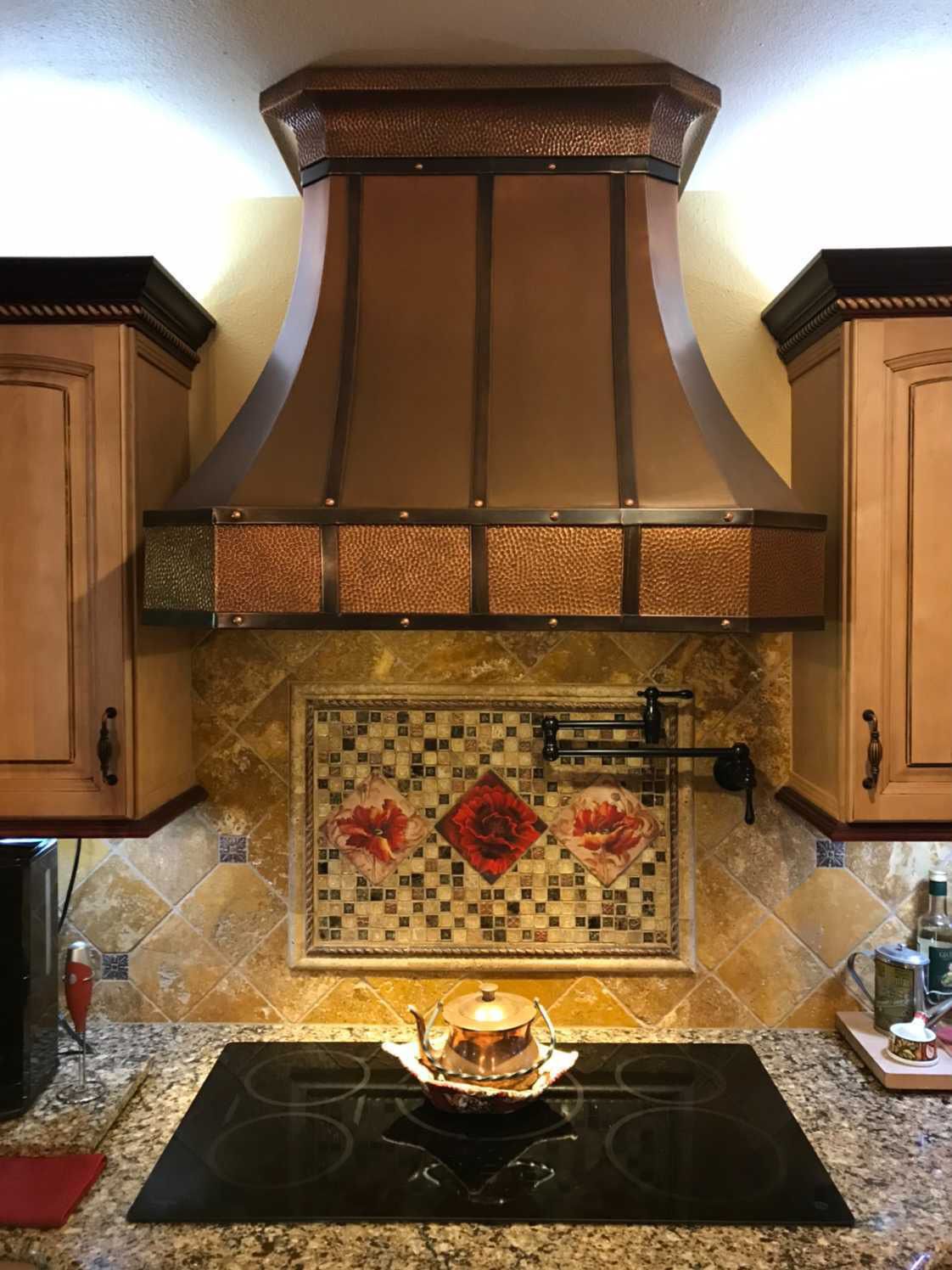 A kitchen with a copper hood over the stove and a mosaic on the wall.