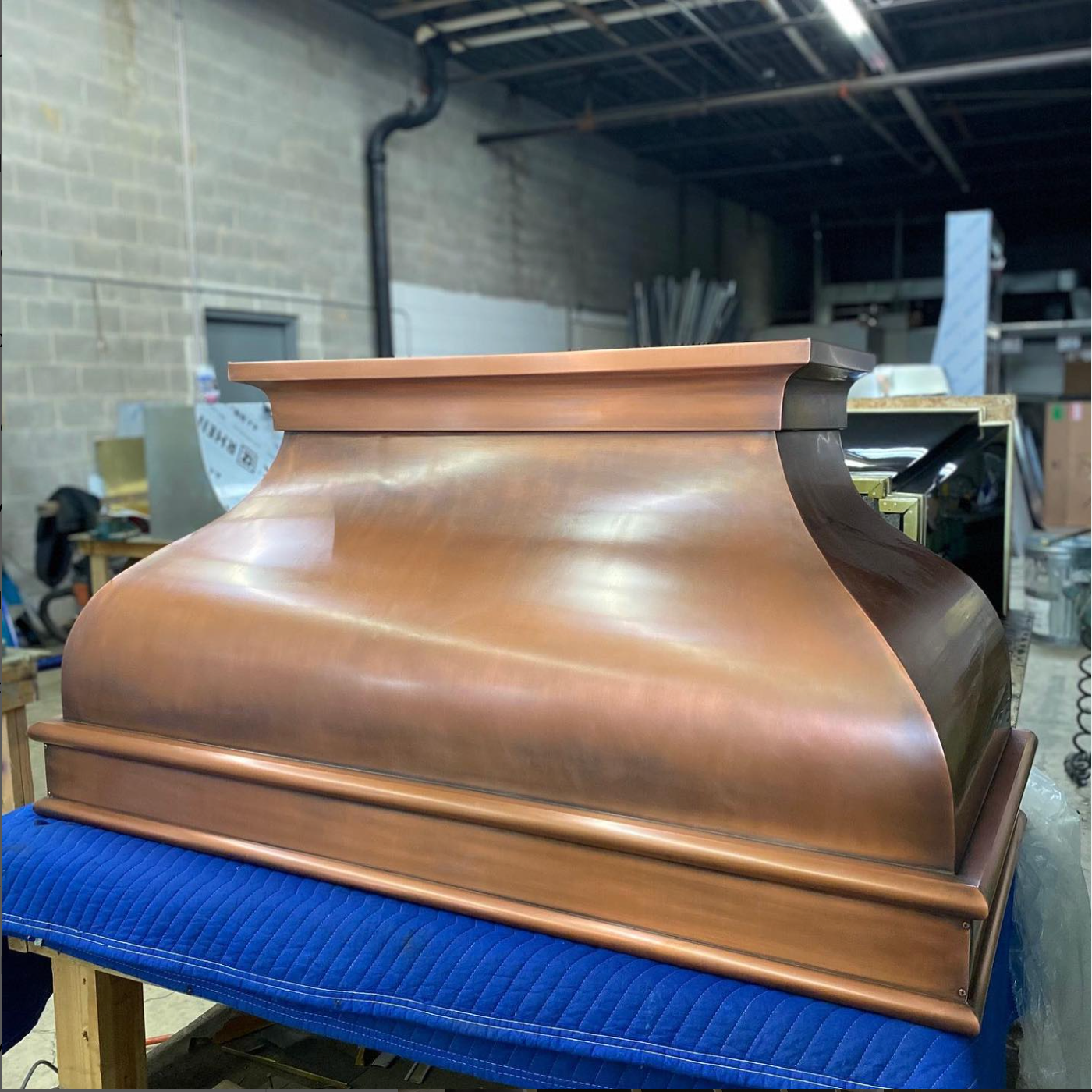 A copper hood is sitting on top of a blue blanket in a room.