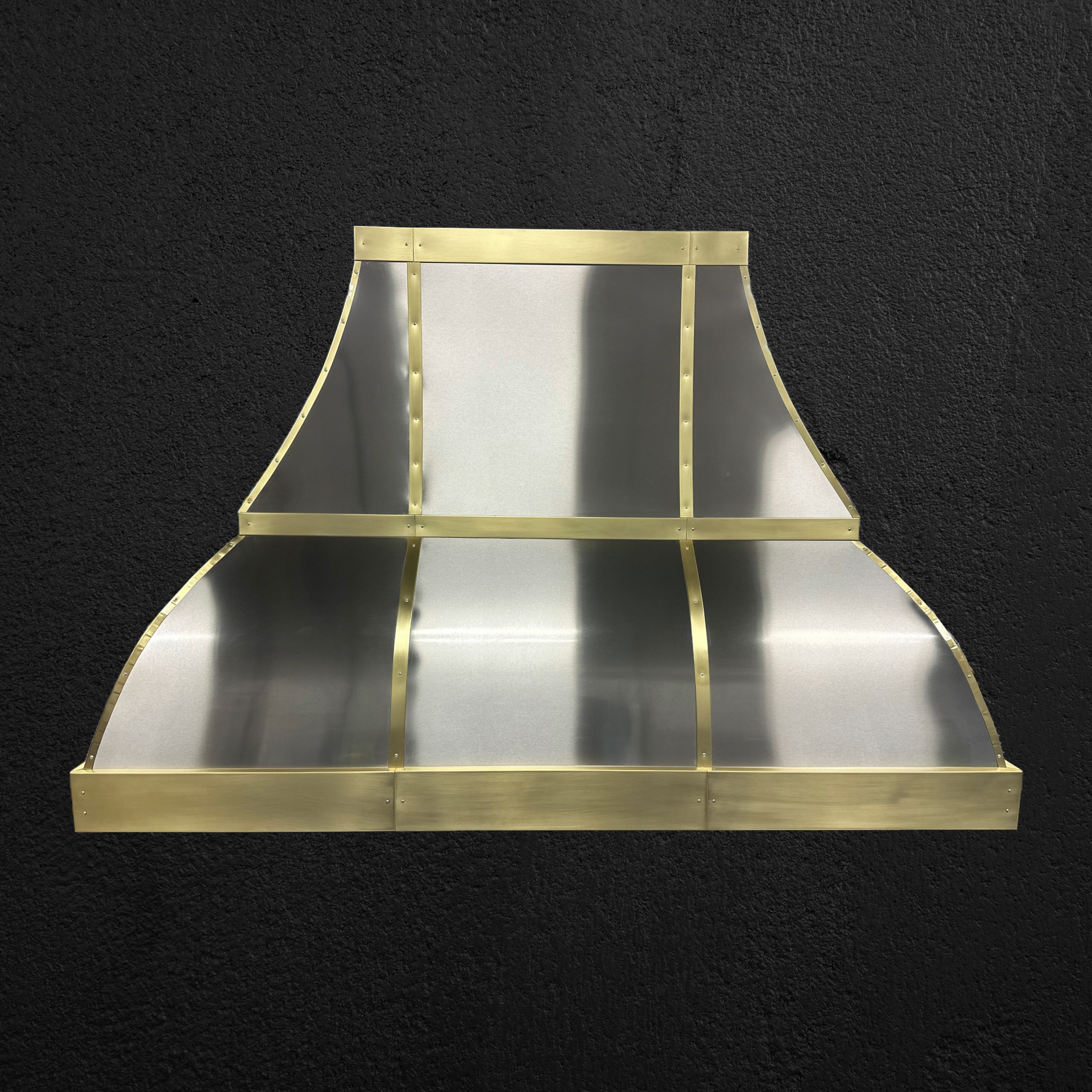 A stainless steel hood with brass trim sits on a black surface