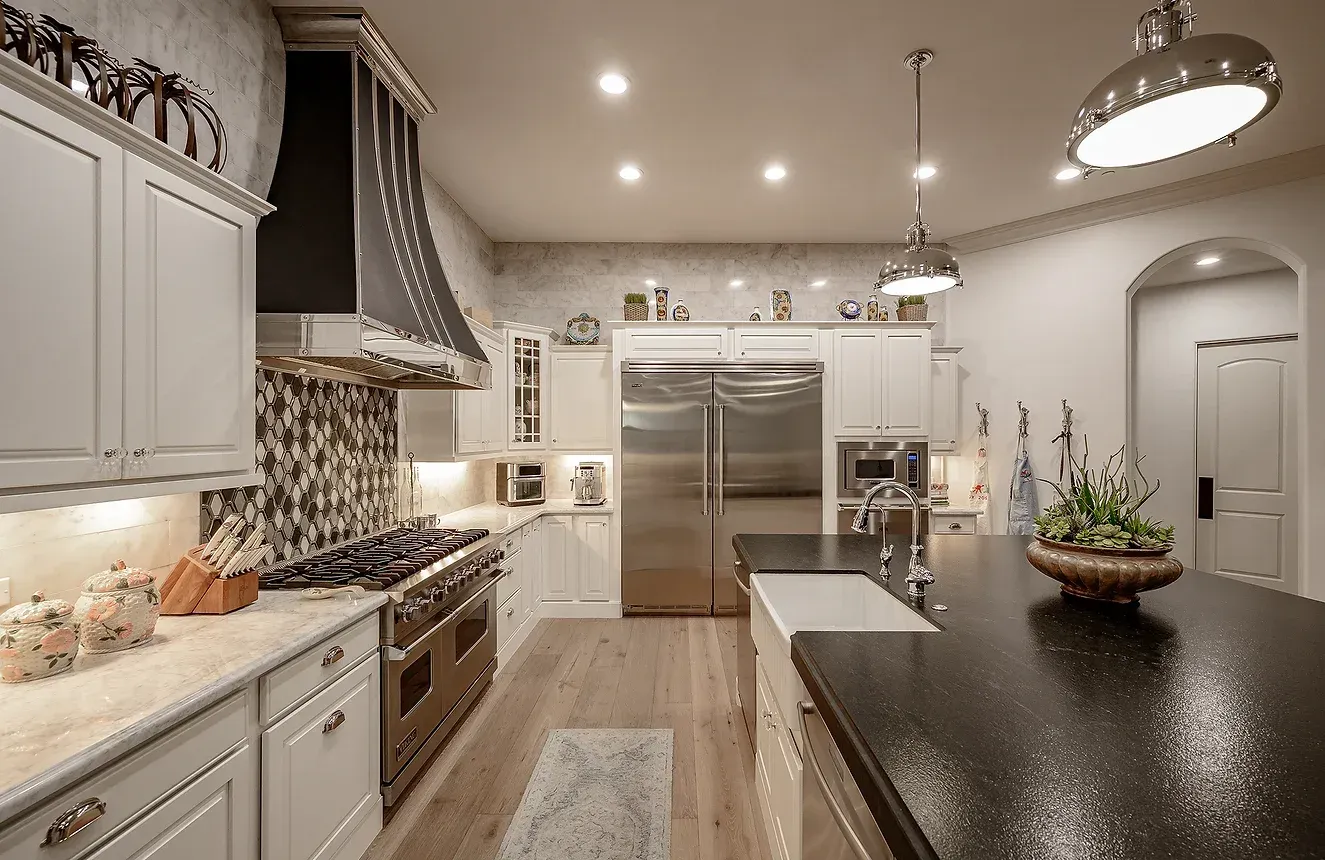 A kitchen with white cabinets , stainless steel appliances , a large island , and a black counter top.
