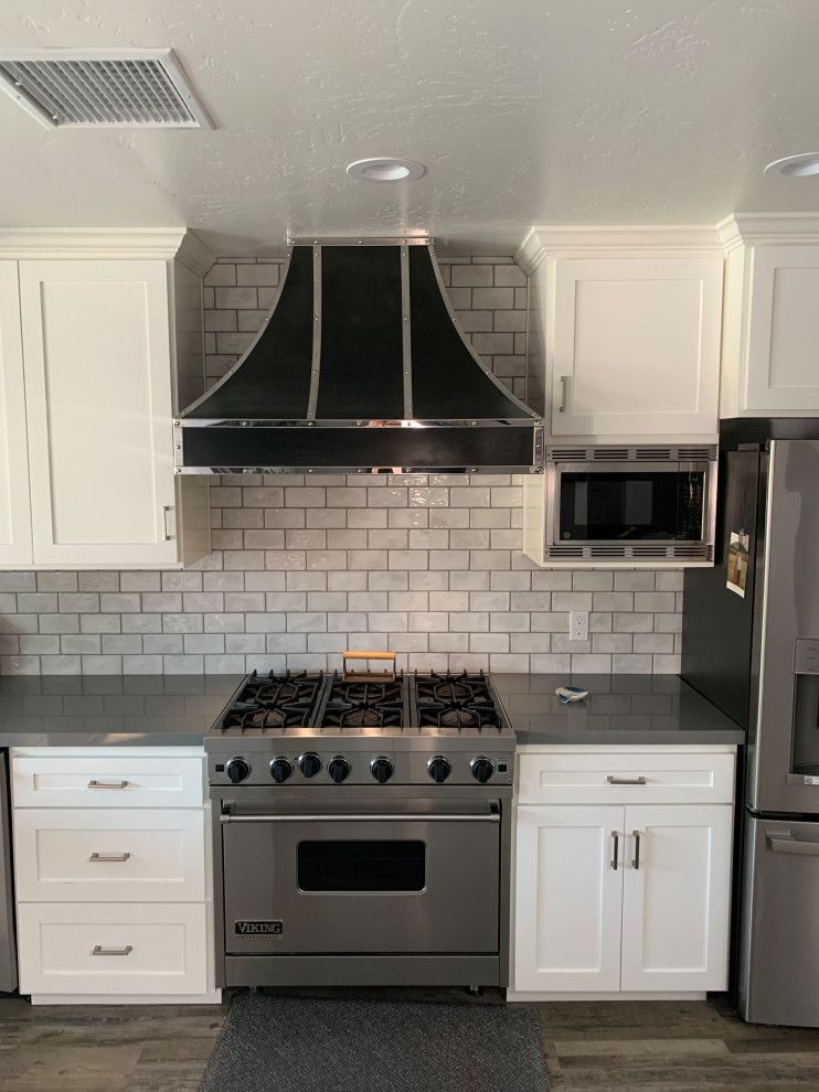 A kitchen with white cabinets , a stove , a refrigerator and a microwave.