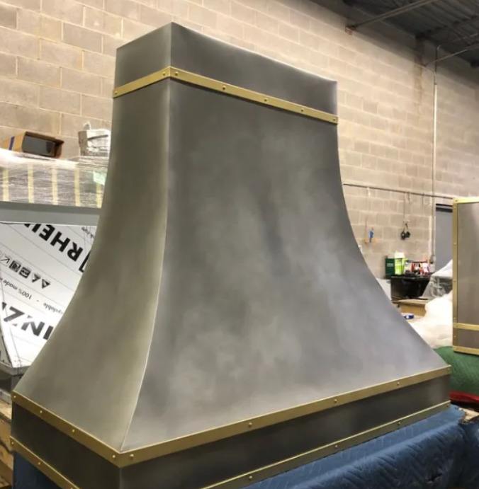 A stainless steel hood with a gold trim sits in a warehouse