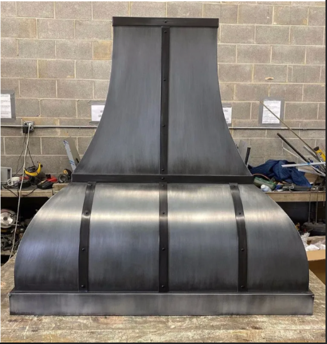 A stainless steel hood is sitting on a wooden table in front of a brick wall