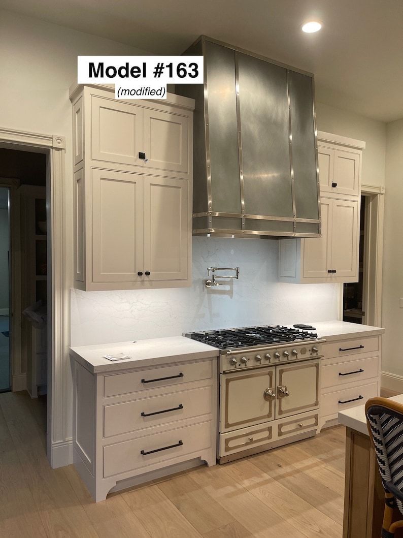 A kitchen with white cabinets , a stove , and a stainless steel hood.