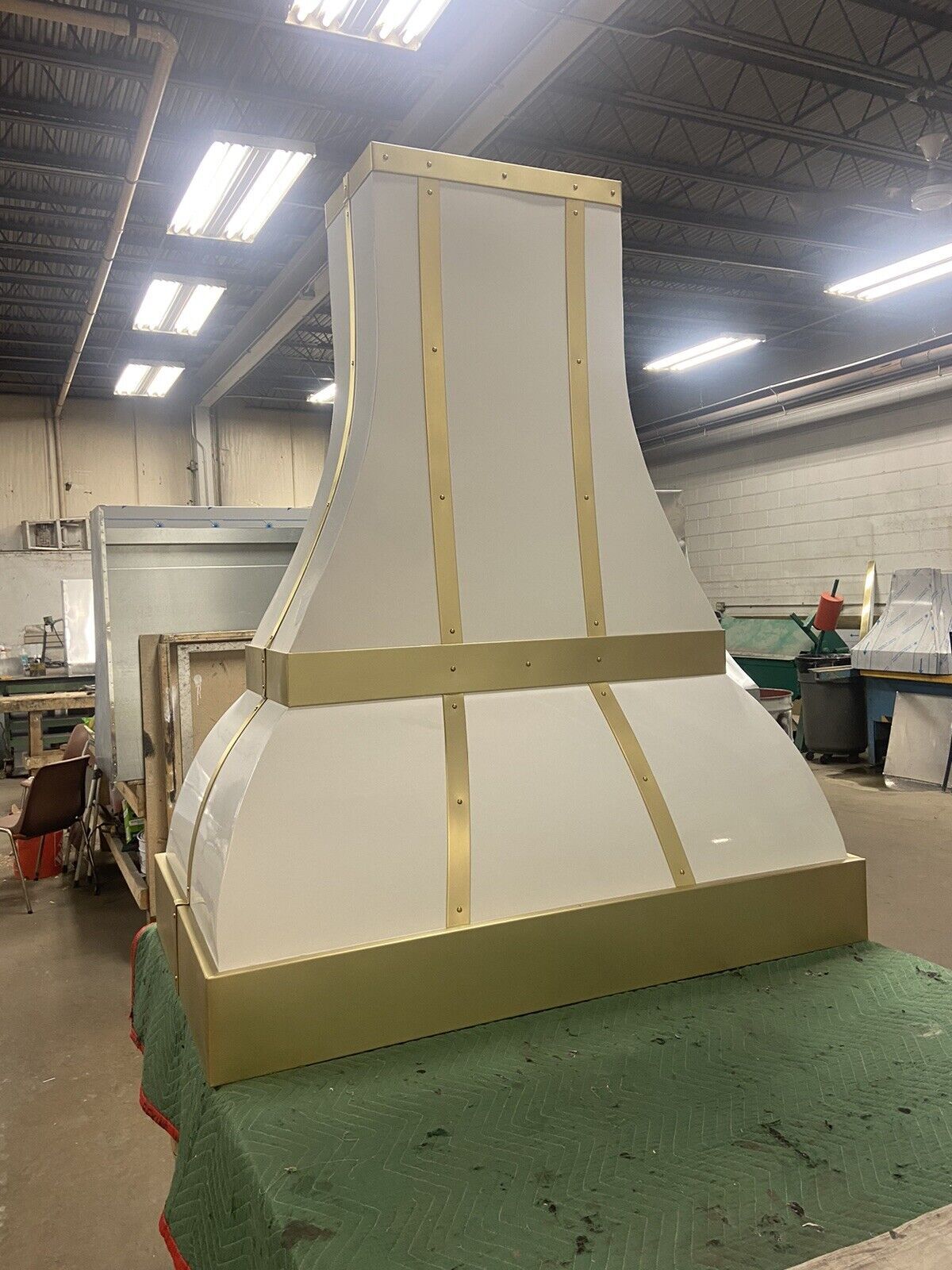 A white and gold hood is sitting on top of a green table in a warehouse.