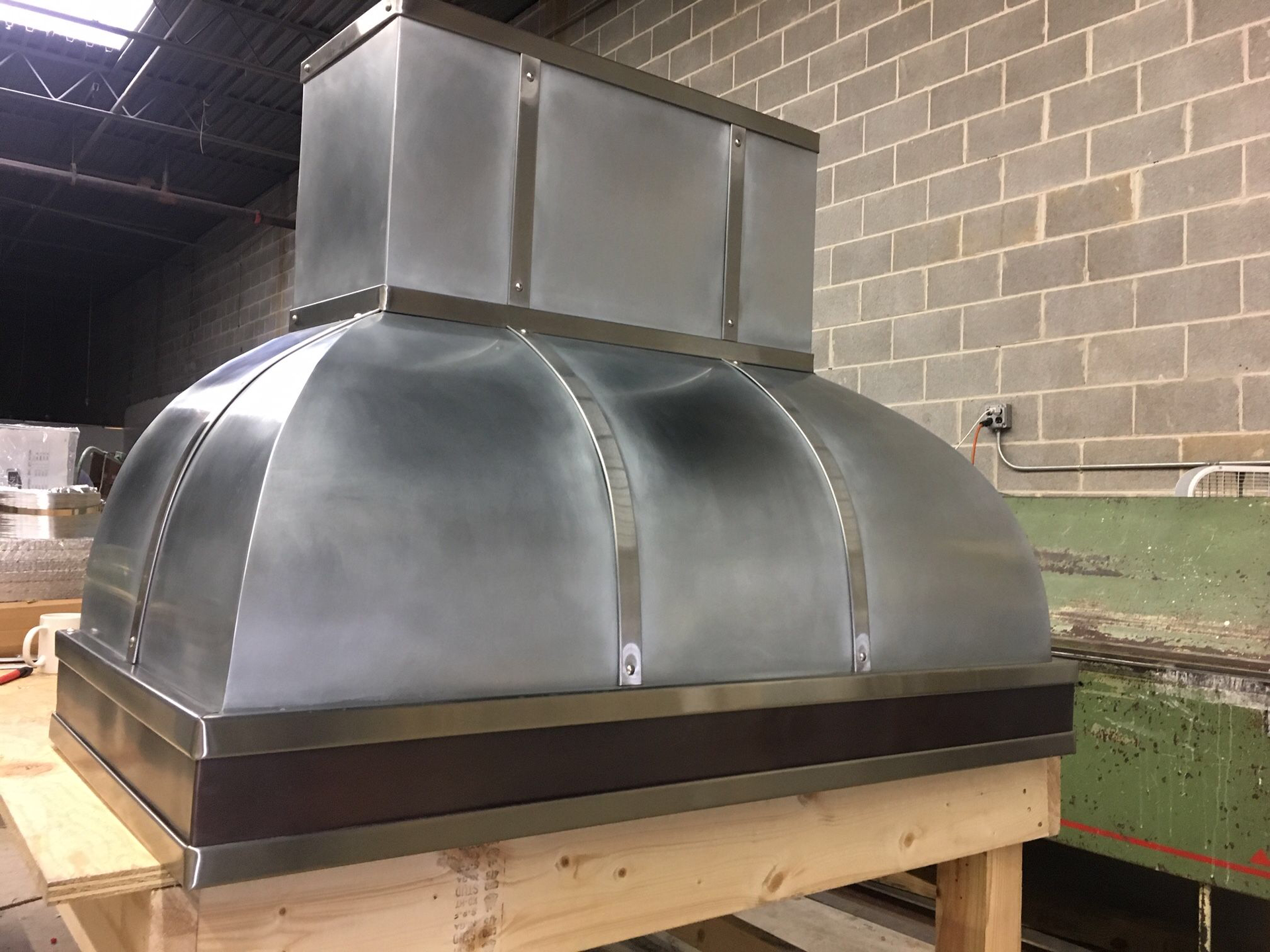 A metal hood is sitting on a wooden table in front of a brick wall.