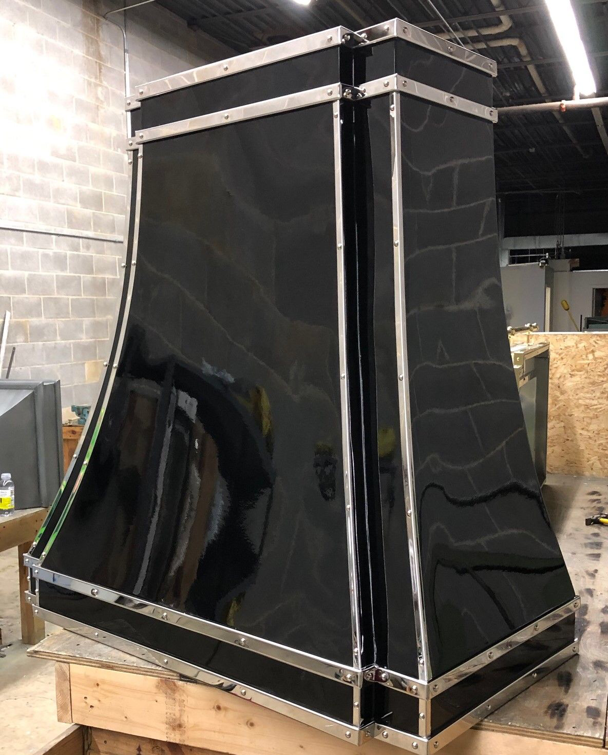 A black stove hood is sitting on top of a wooden pallet in a warehouse.