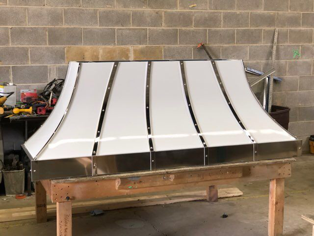 A stainless steel hood is sitting on a wooden table in front of a brick wall.