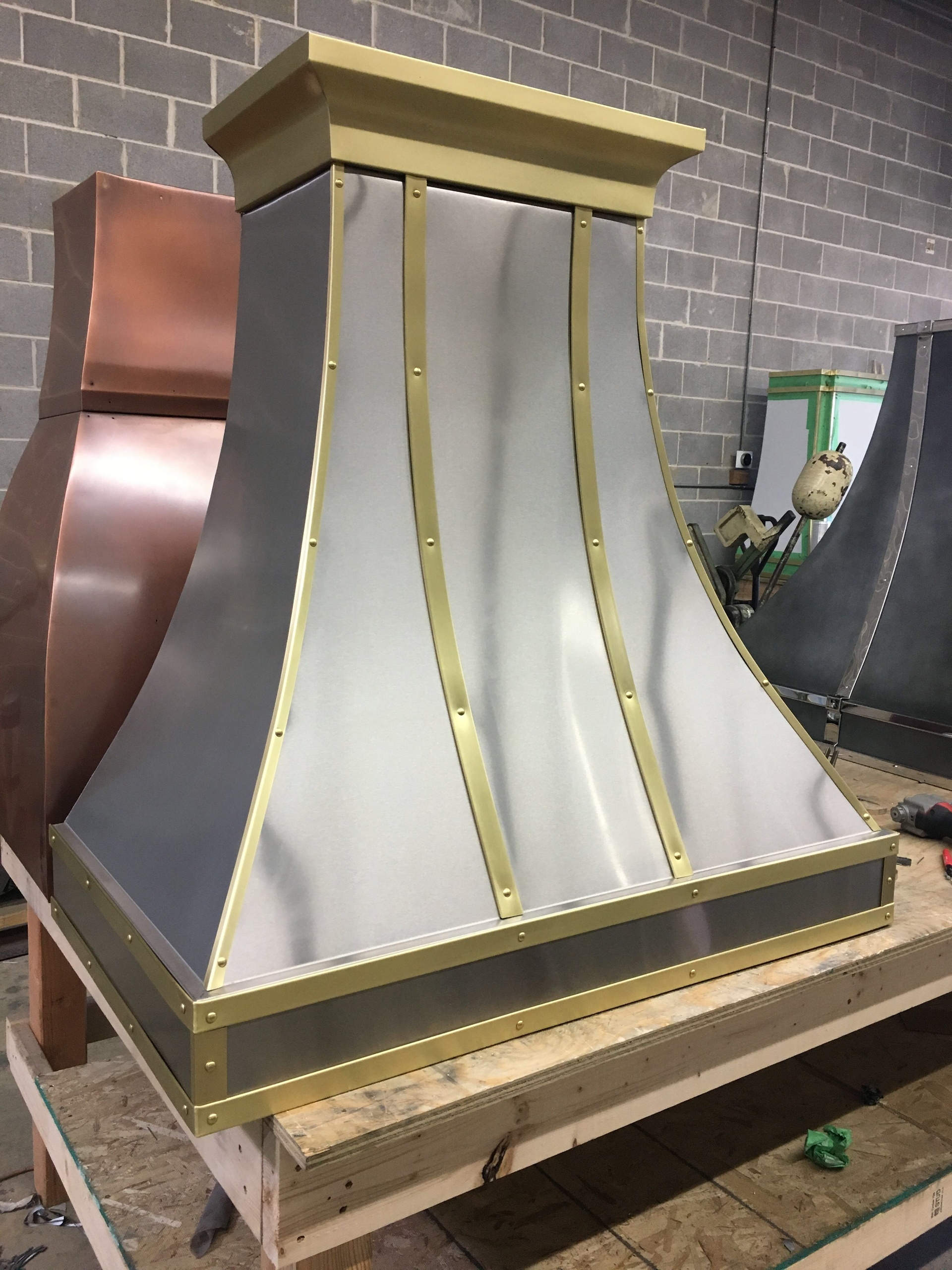 A stainless steel hood with gold trim is sitting on a wooden table.