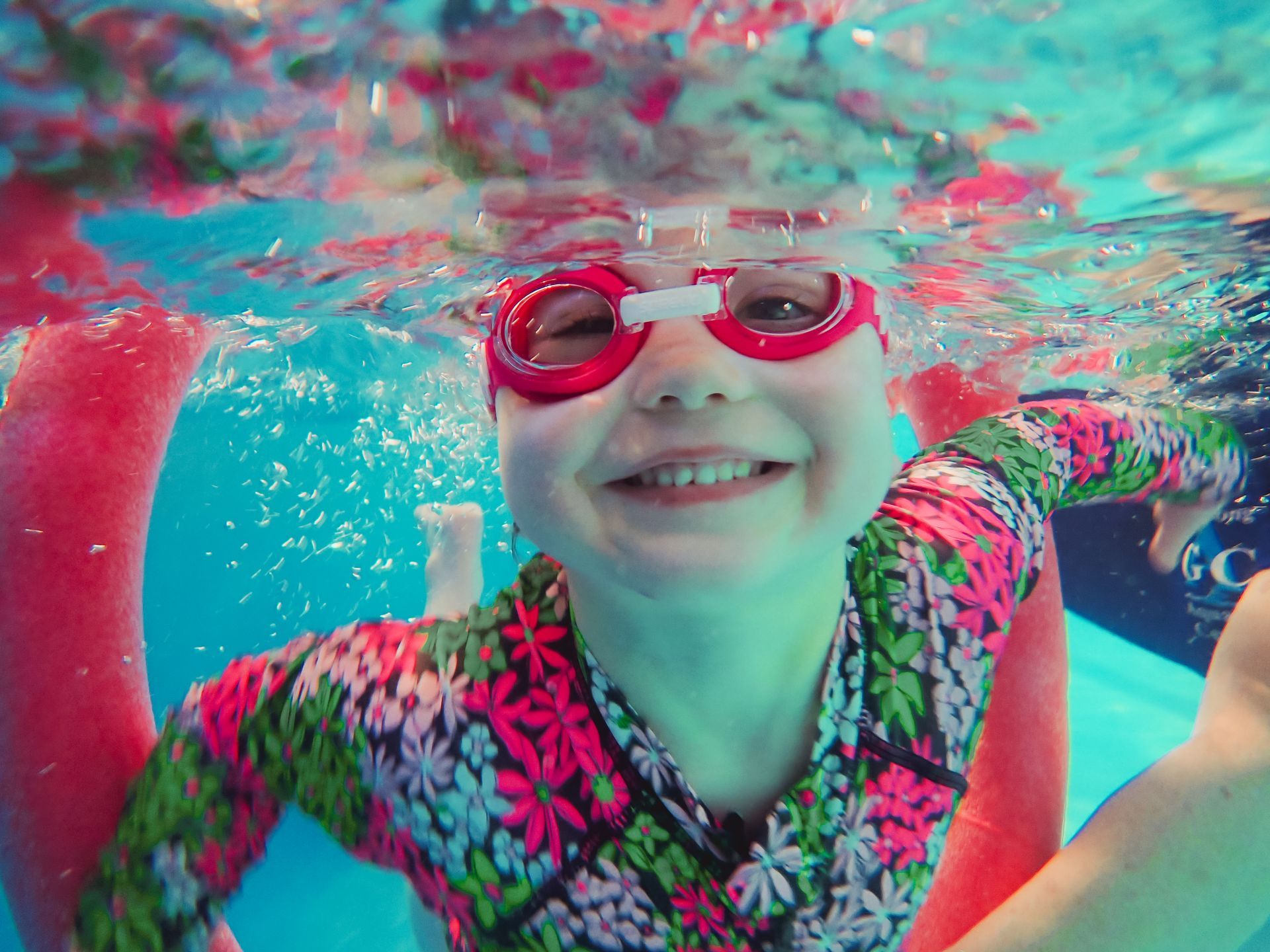A little girl wearing goggles is swimming underwater in a pool.