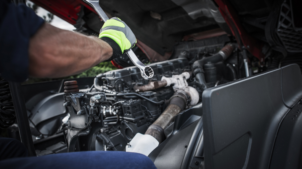 Mechanic working on a car engine in a workshop, using tools amid exposed engine components.