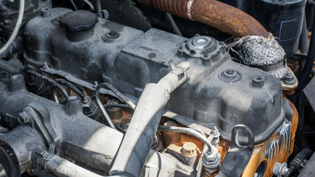 Dusty engine bay with rusted car parts and a hose