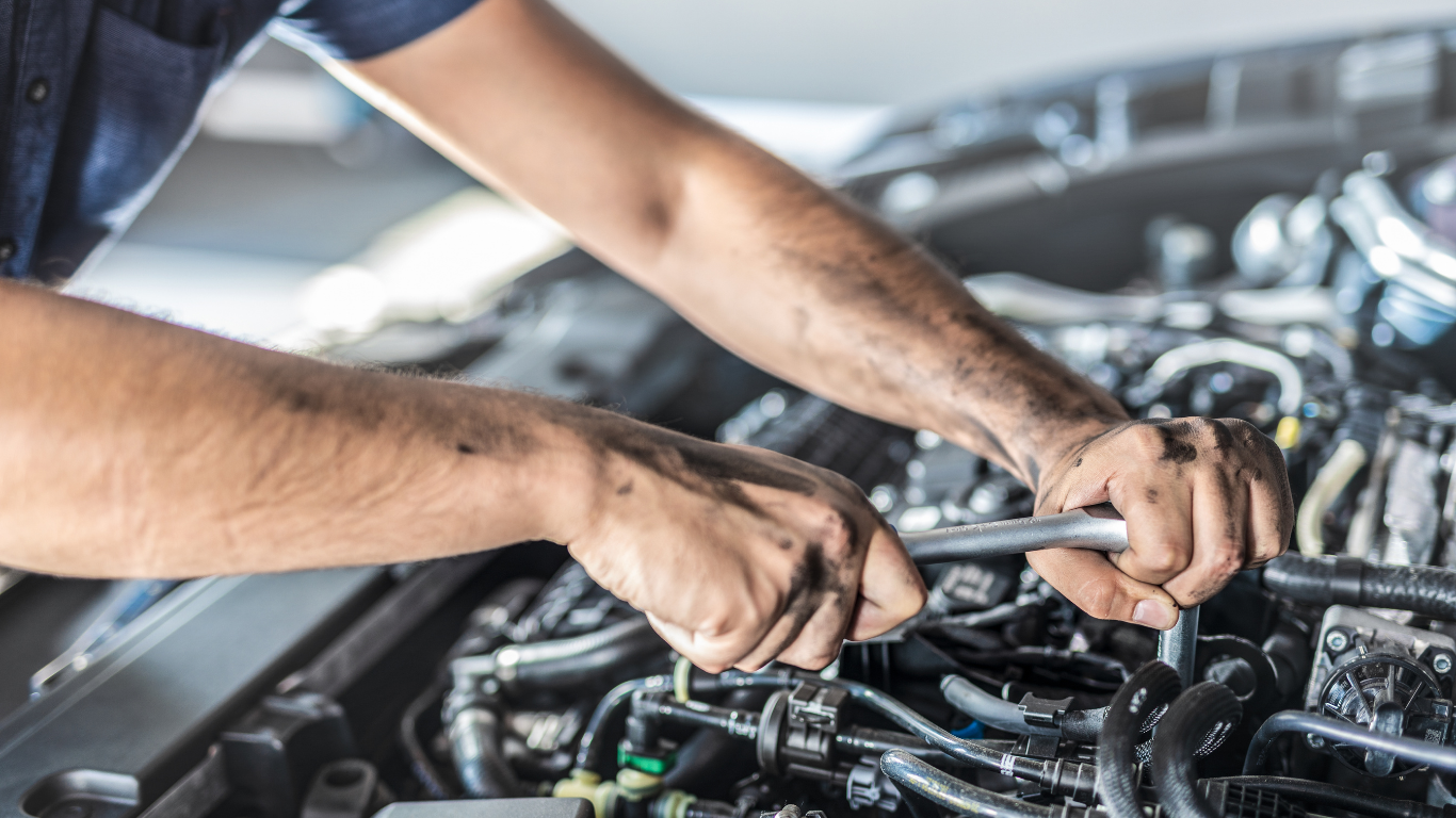 Mechanic working on a car engine in a garage, tightening hoses with both hands.