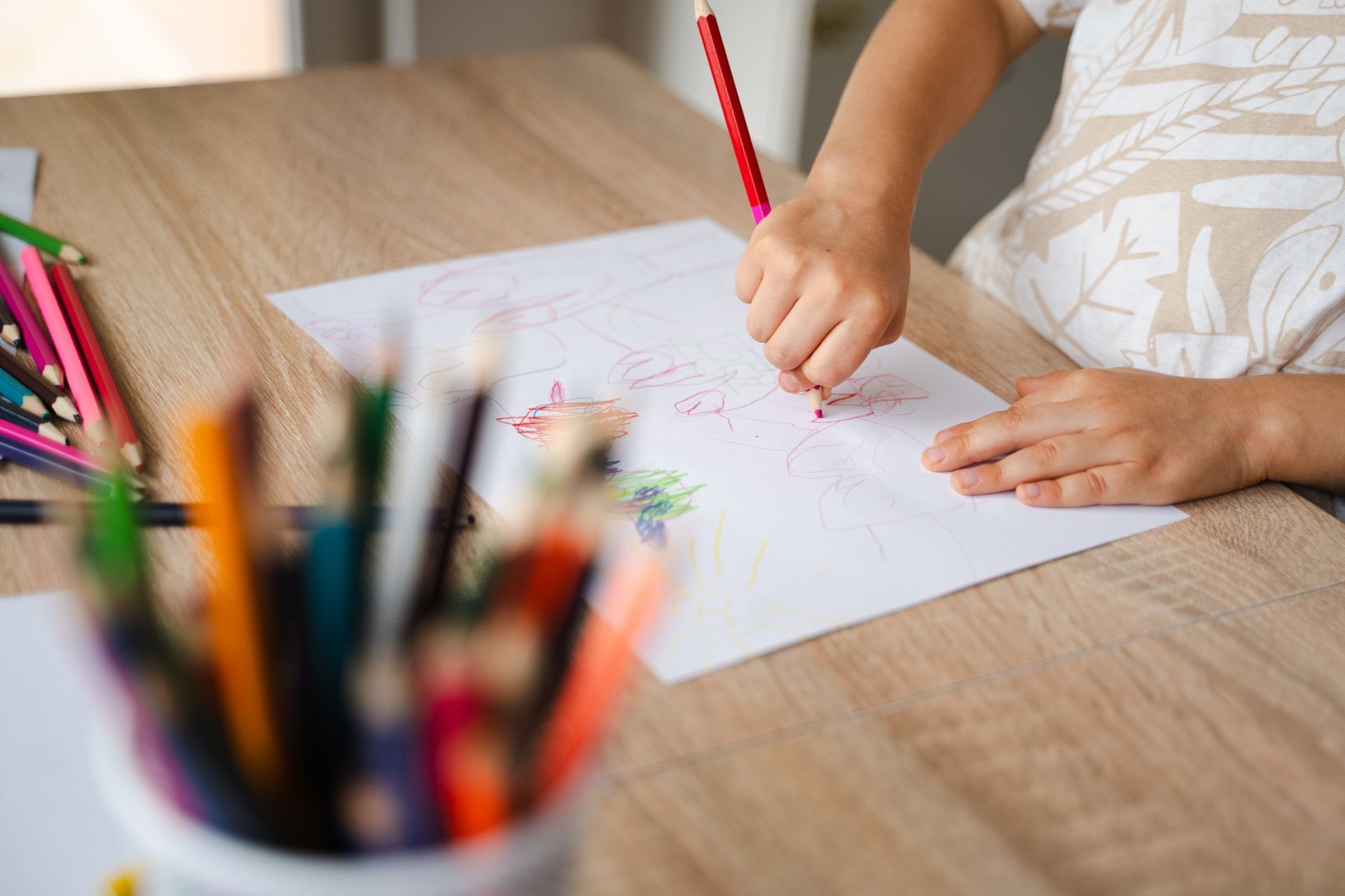 A child is sitting at a table drawing with a pencil.