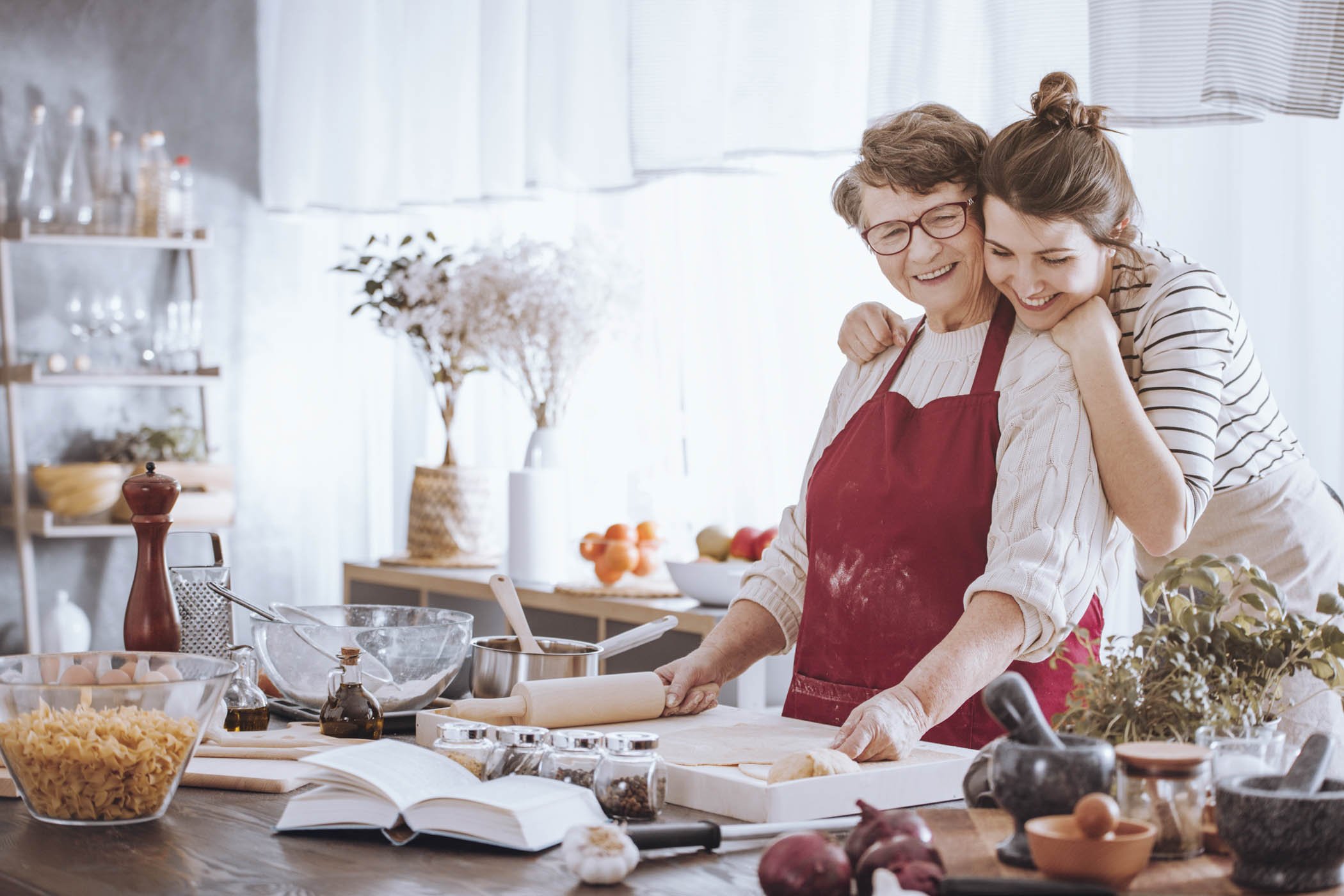 Granddaughter hugging grandmother while making cake together in the kitchen