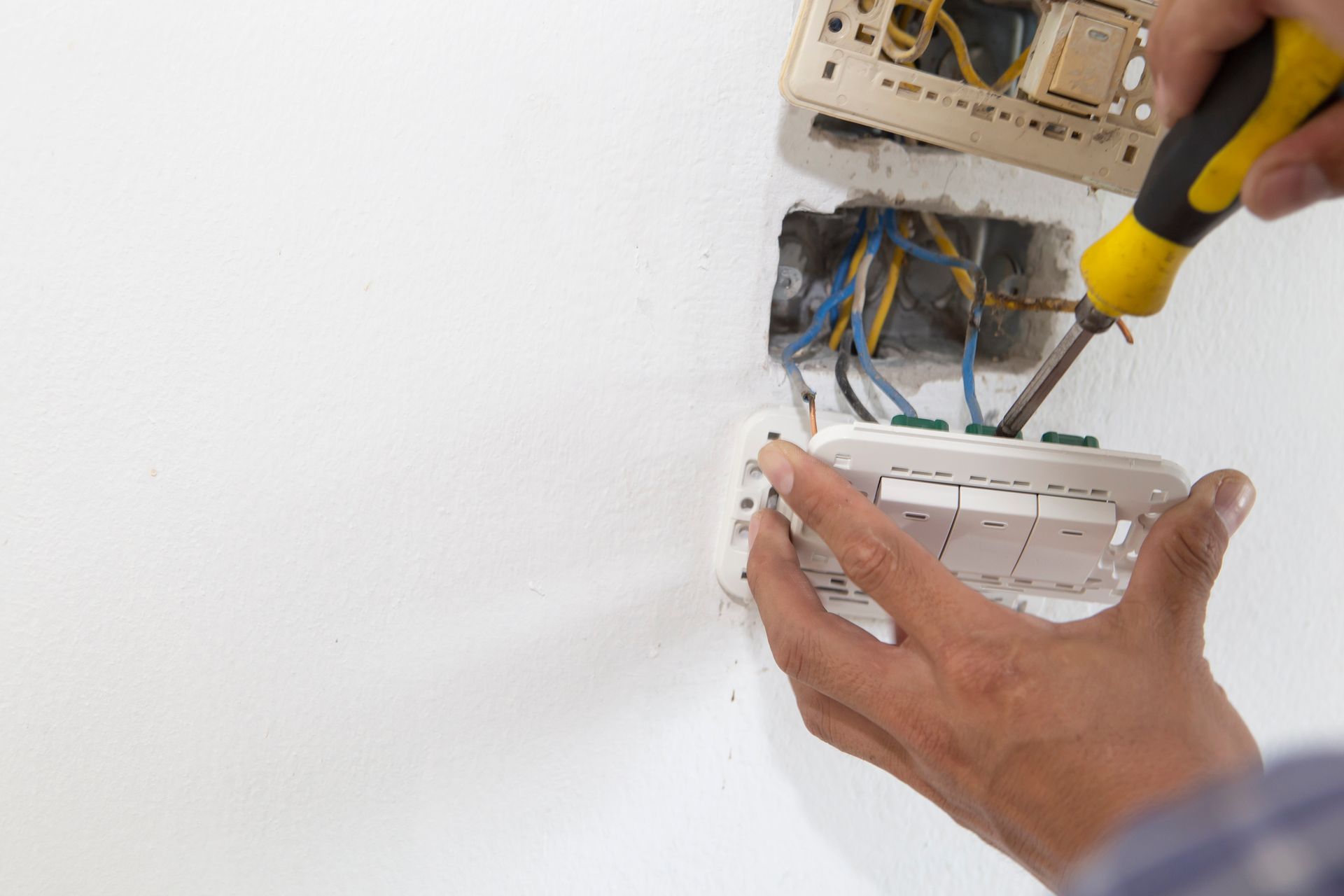 Person installing a light switch on a white wall 