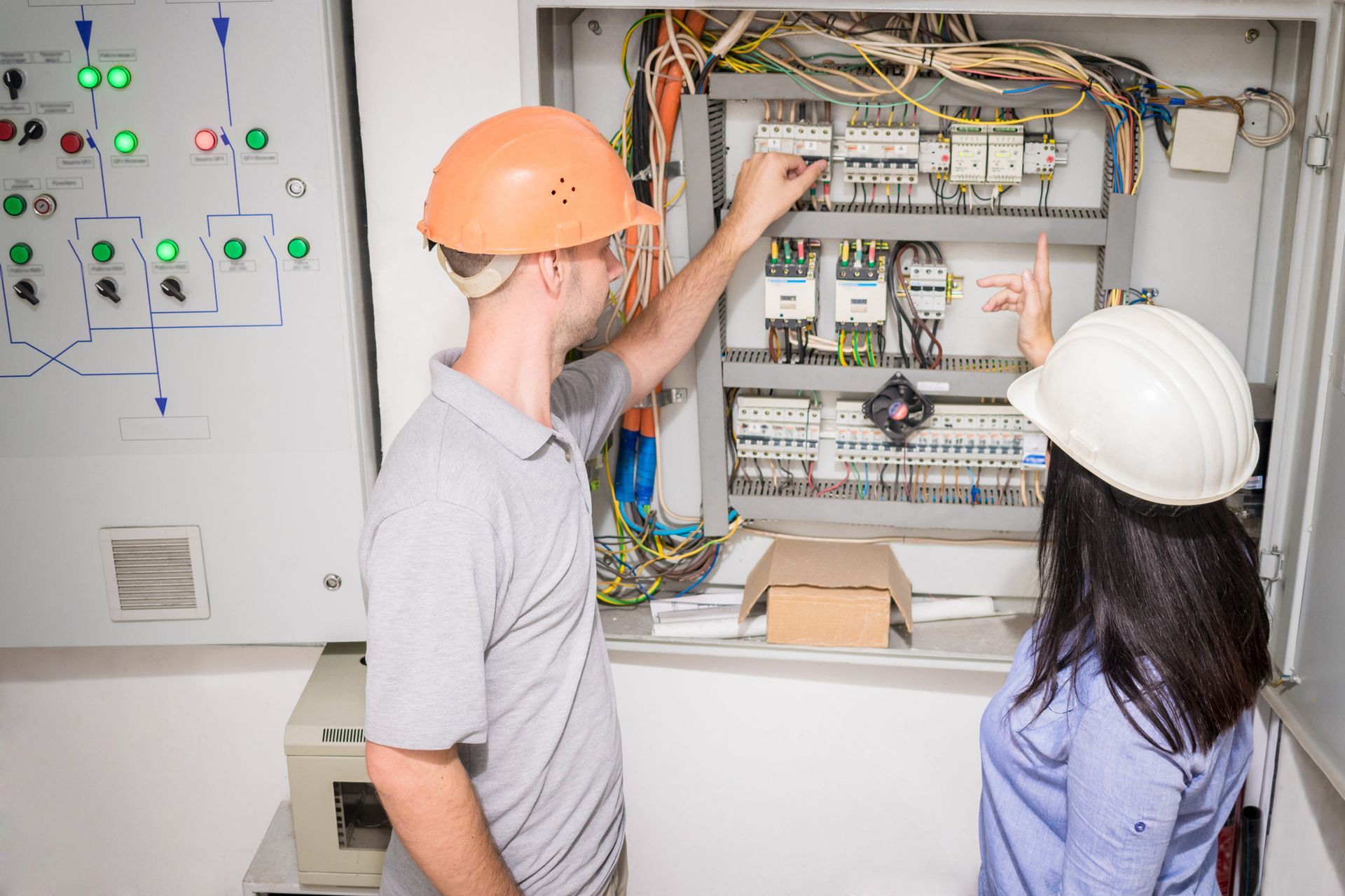 Two people in hard hats inspecting electrical panel