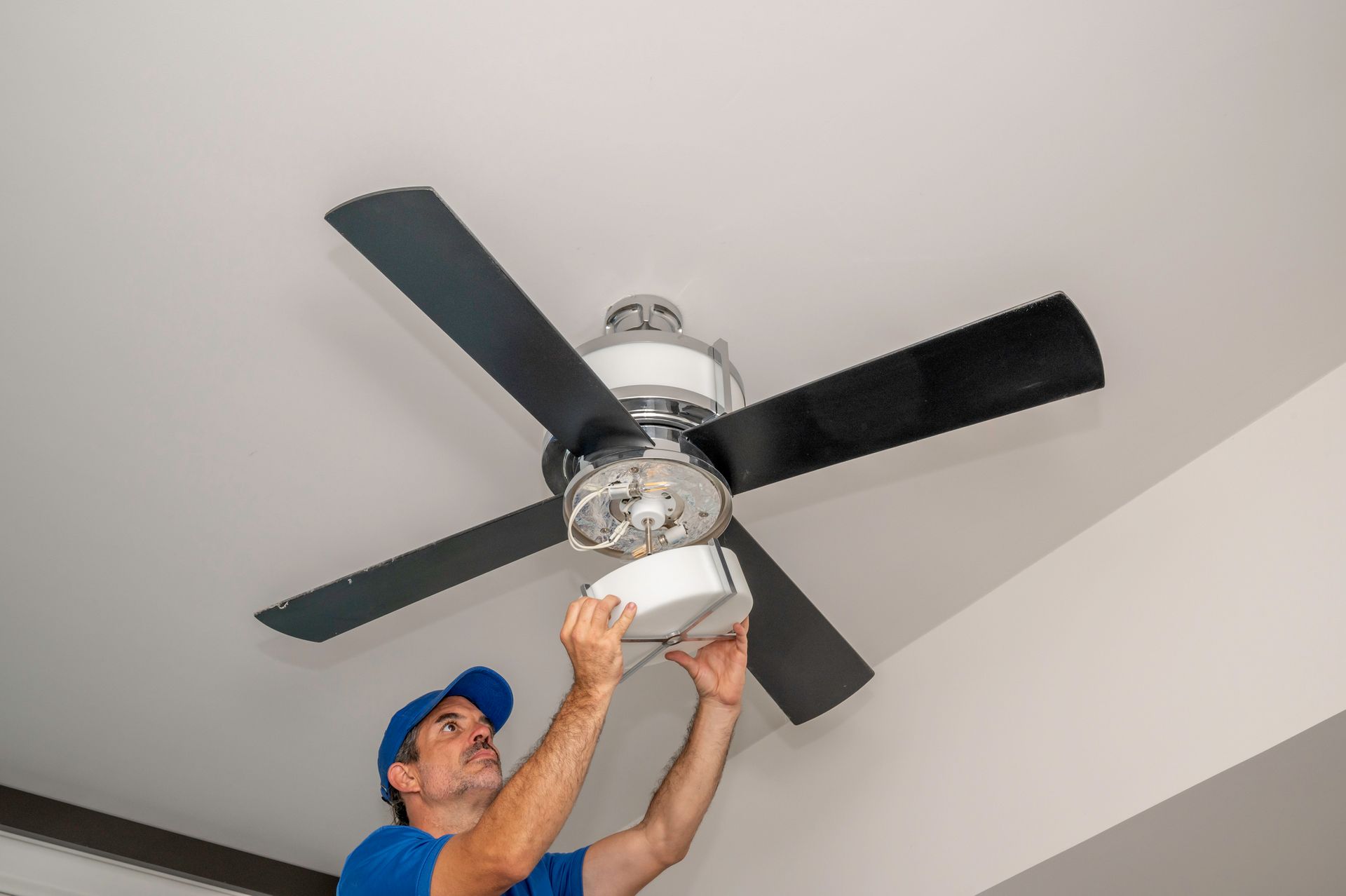 Electrician is installing a ceiling fan with a light fixture.