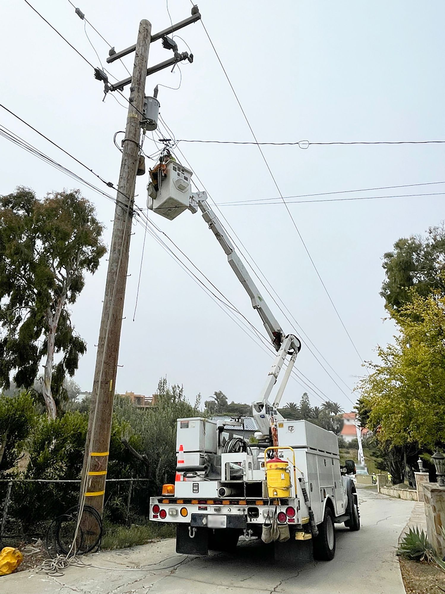 Utility worker in a bucket truck repairs power lines on a utility pole on a residential street