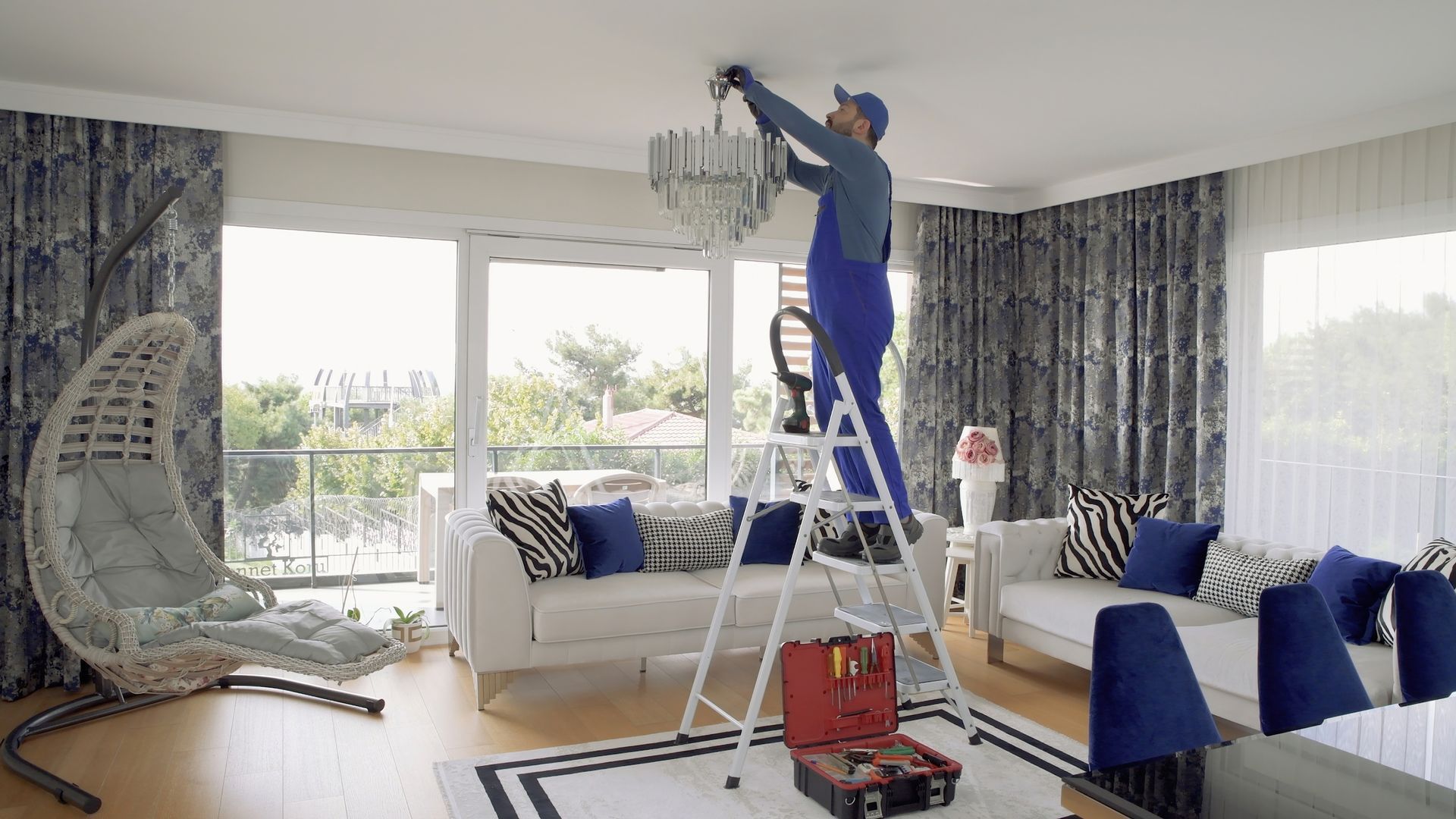 Electrician on a ladder is installing a chandelier in a living room Electrician on a ladder is installing a chandelier in a living room