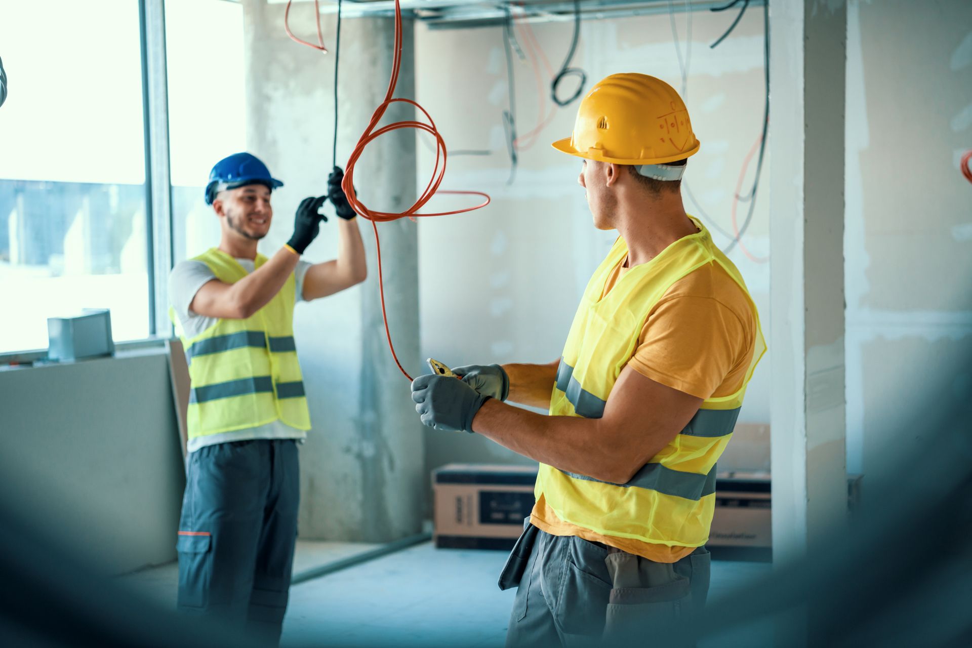 Two construction workers are installing wiring in a building under construction.