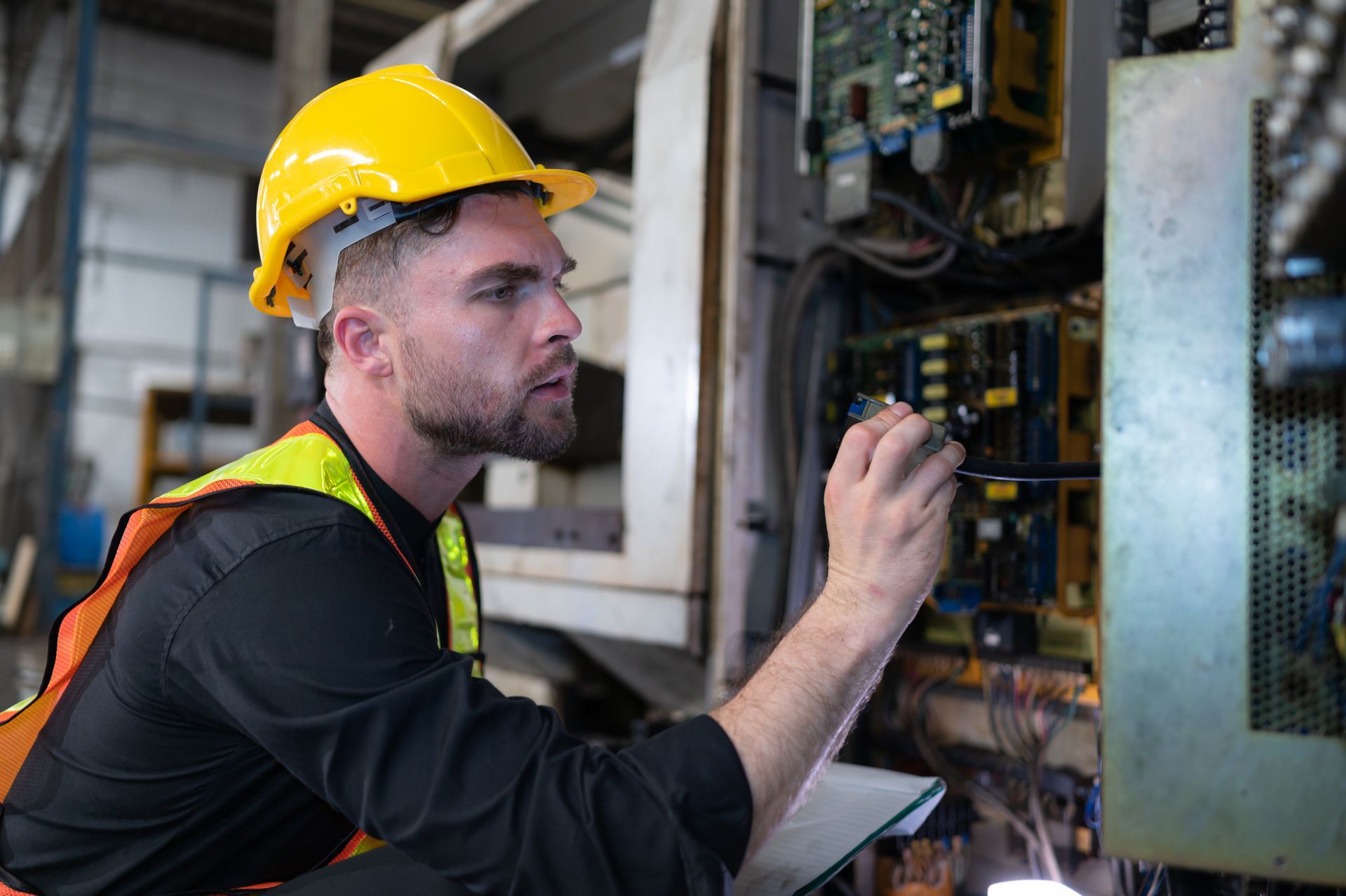 A man in a yellow hard hat and safety vest is examining the machinery's electrical components