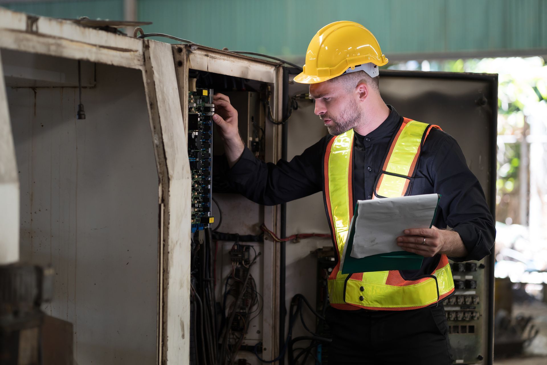 An electrician inspects electrical equipment, holding a clipboard.