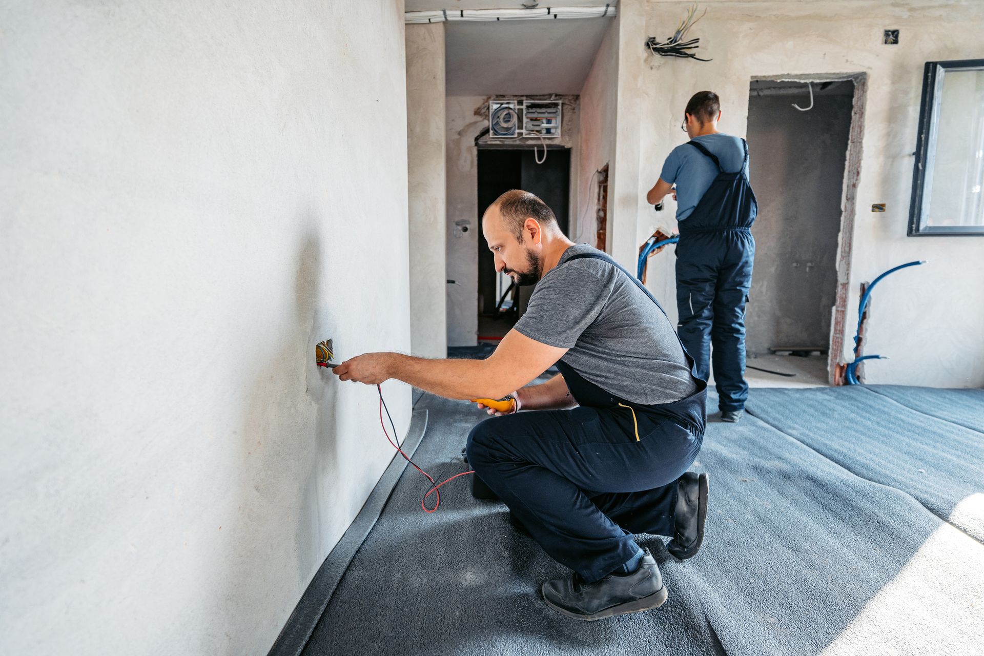 Two workers are installing electrical outlets in a room under construction