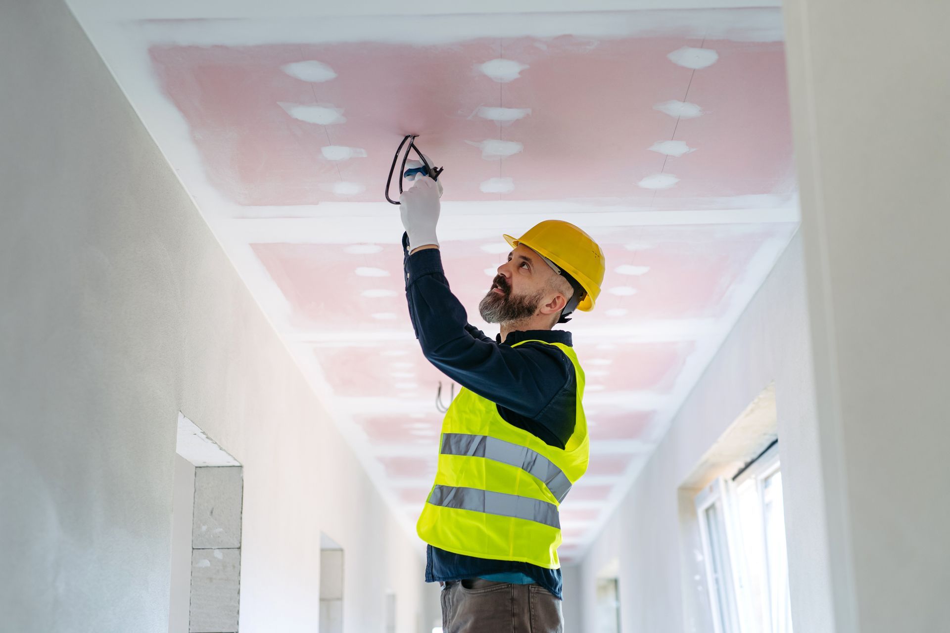 Construction worker in a yellow hard hat and vest works on the ceiling