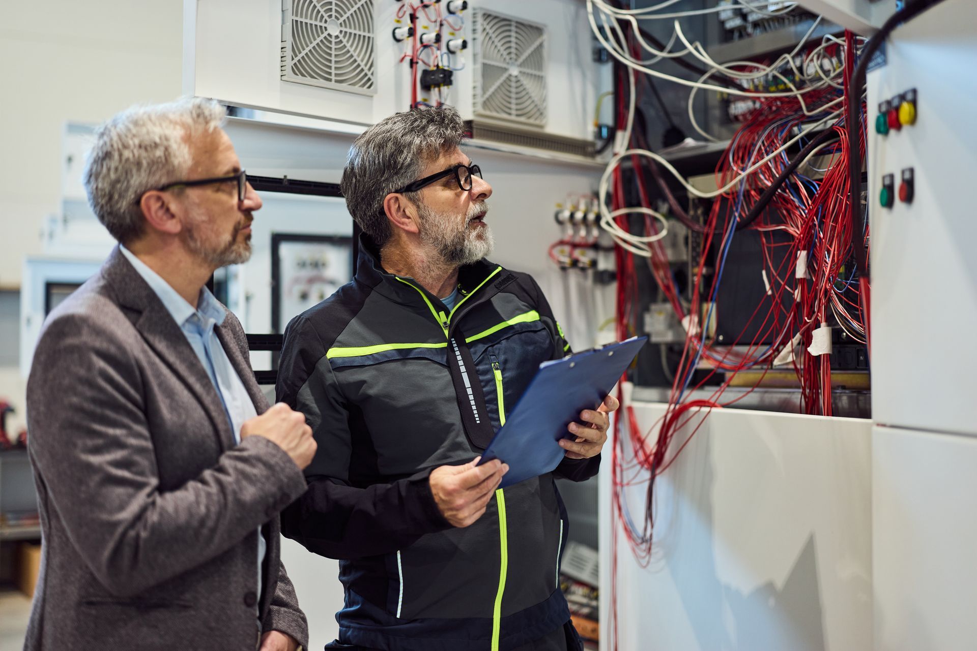 Two men are examining electrical wiring in a machinery cabinet