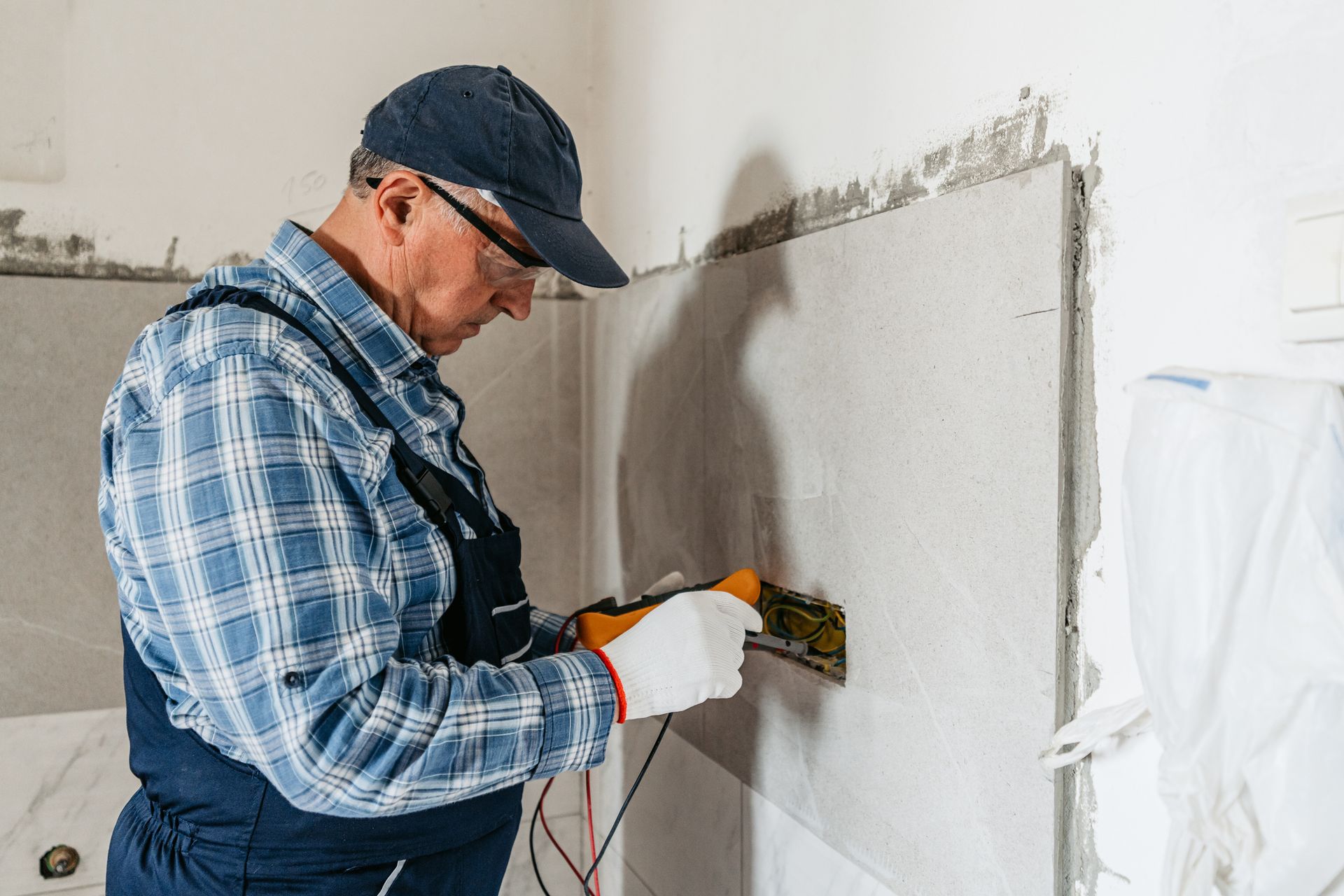 Electrician checking an electrical outlet on a wall, wearing safety glasses and gloves Electrician checking an electrical outlet on a wall, wearing safety glasses and gloves