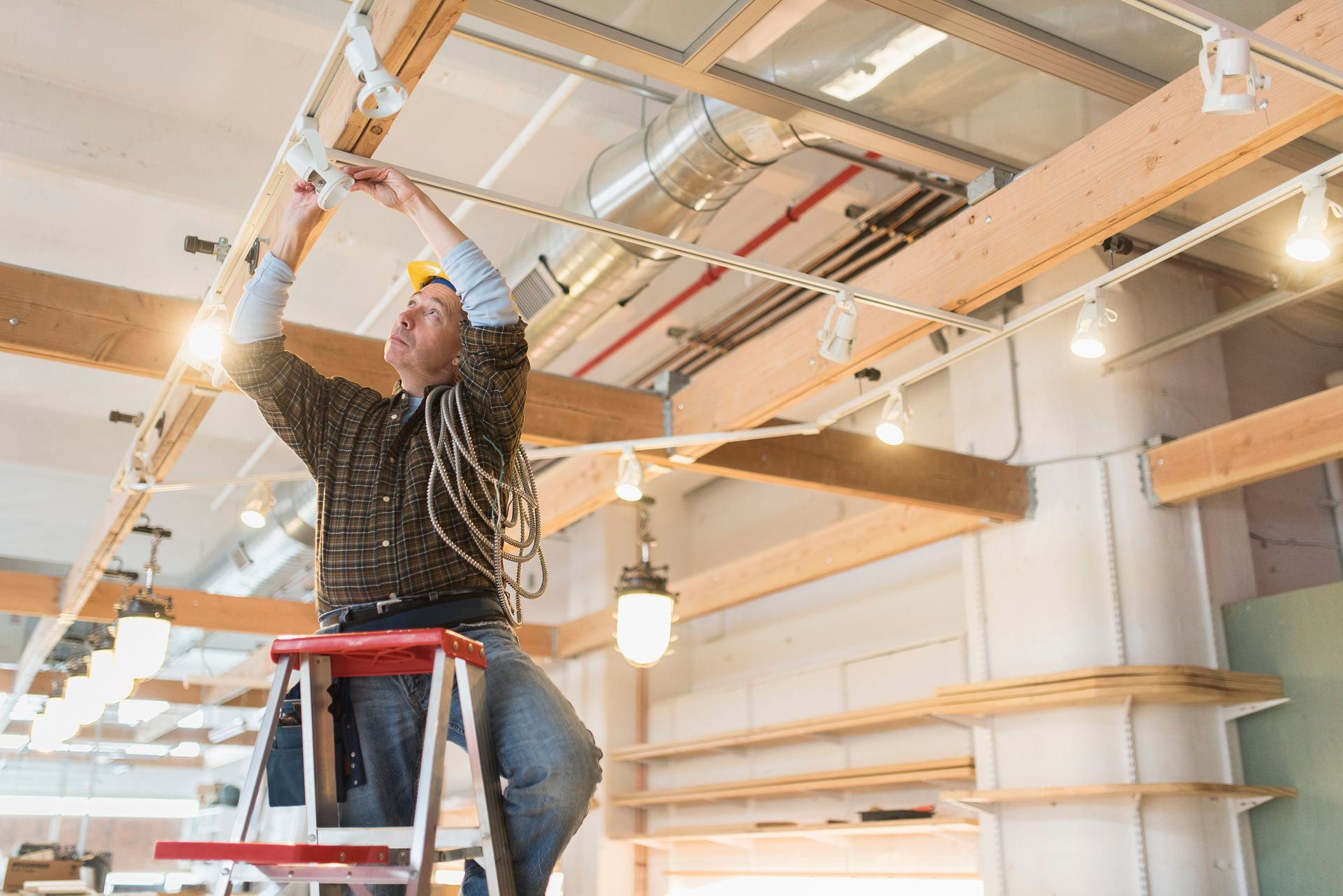 Electrician on a ladder installs lighting in a building