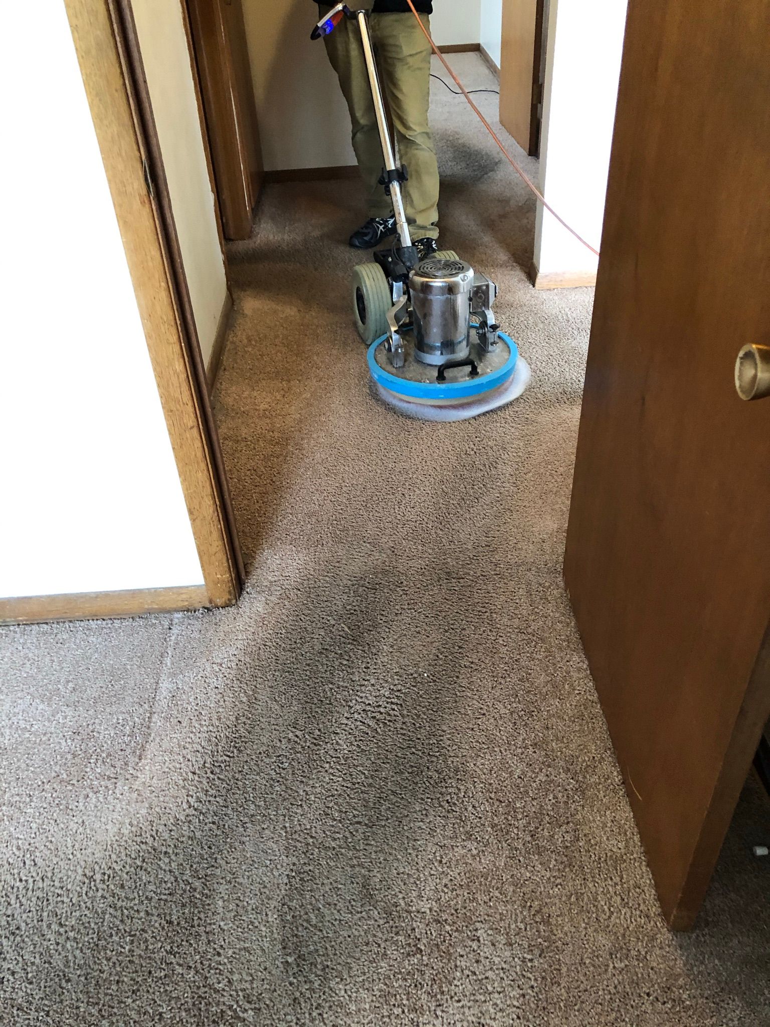 A person is cleaning a carpet with a machine in a hallway.