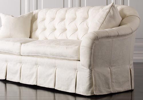 A white couch with pillows on it is sitting on a wooden floor.