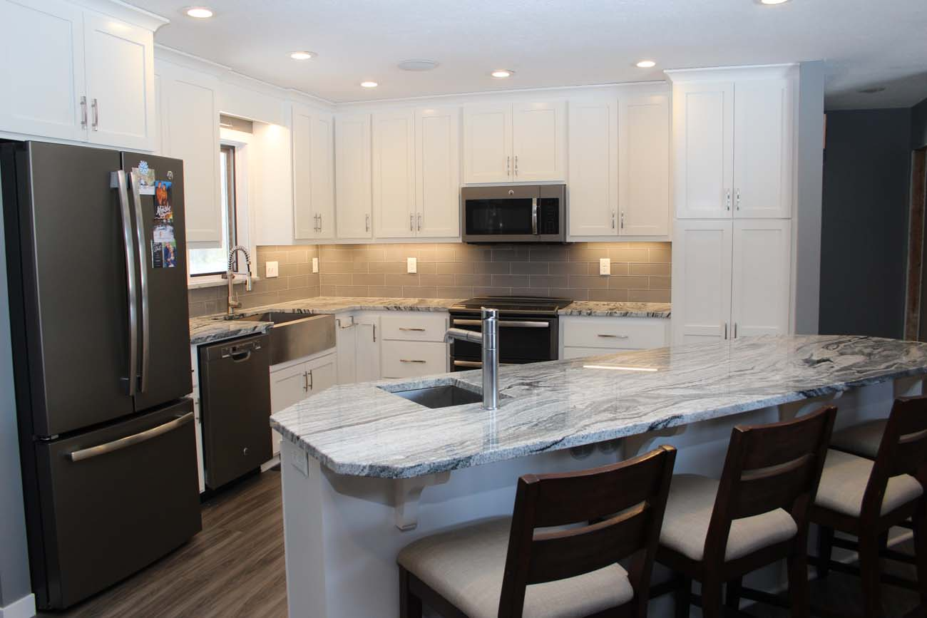 A kitchen with white cabinets , granite counter tops , stainless steel appliances and a large island.