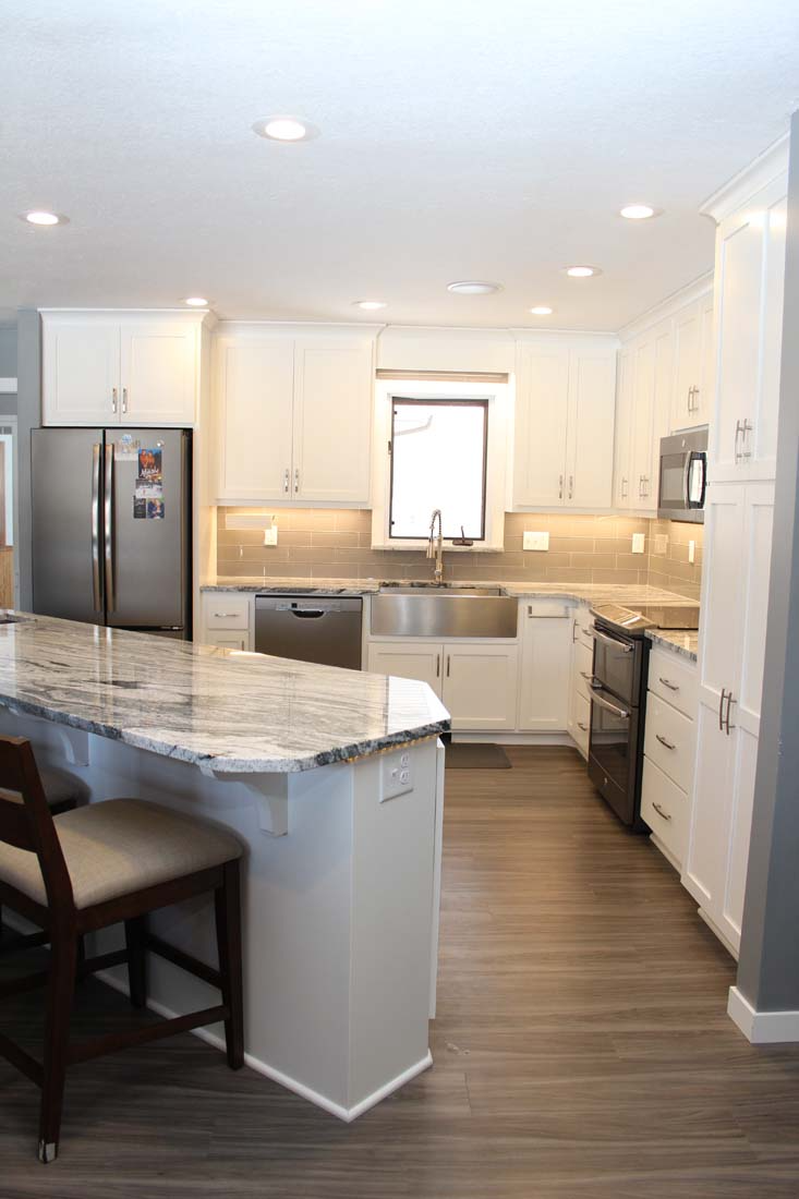 A kitchen with white cabinets , granite counter tops , stainless steel appliances and a large island.
