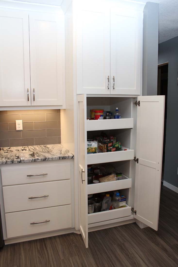 A kitchen with white cabinets and drawers and a pantry with the door open.