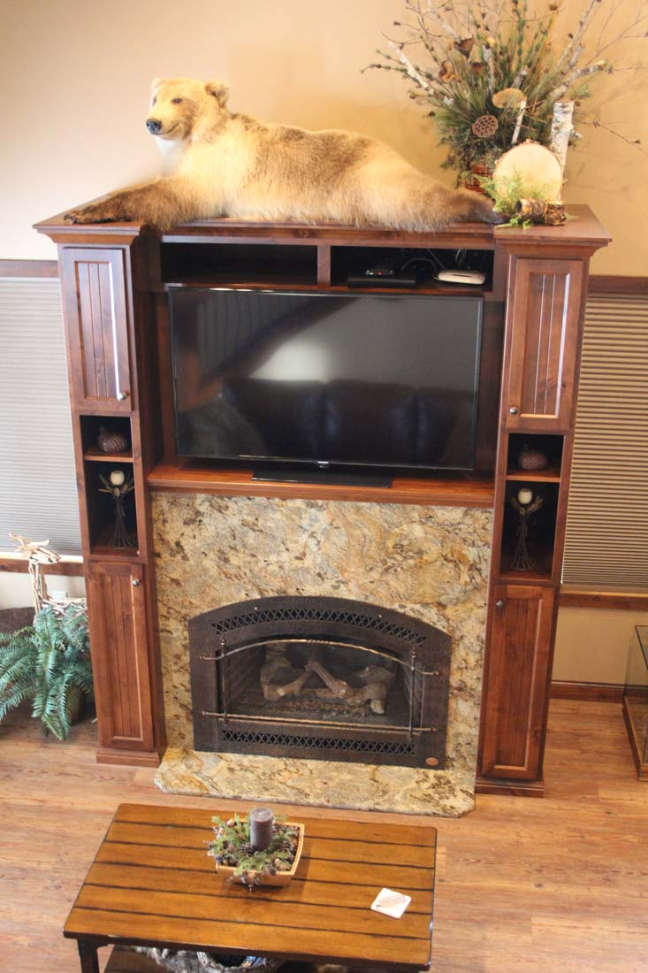 A dog is laying on top of a wooden entertainment center next to a fireplace.