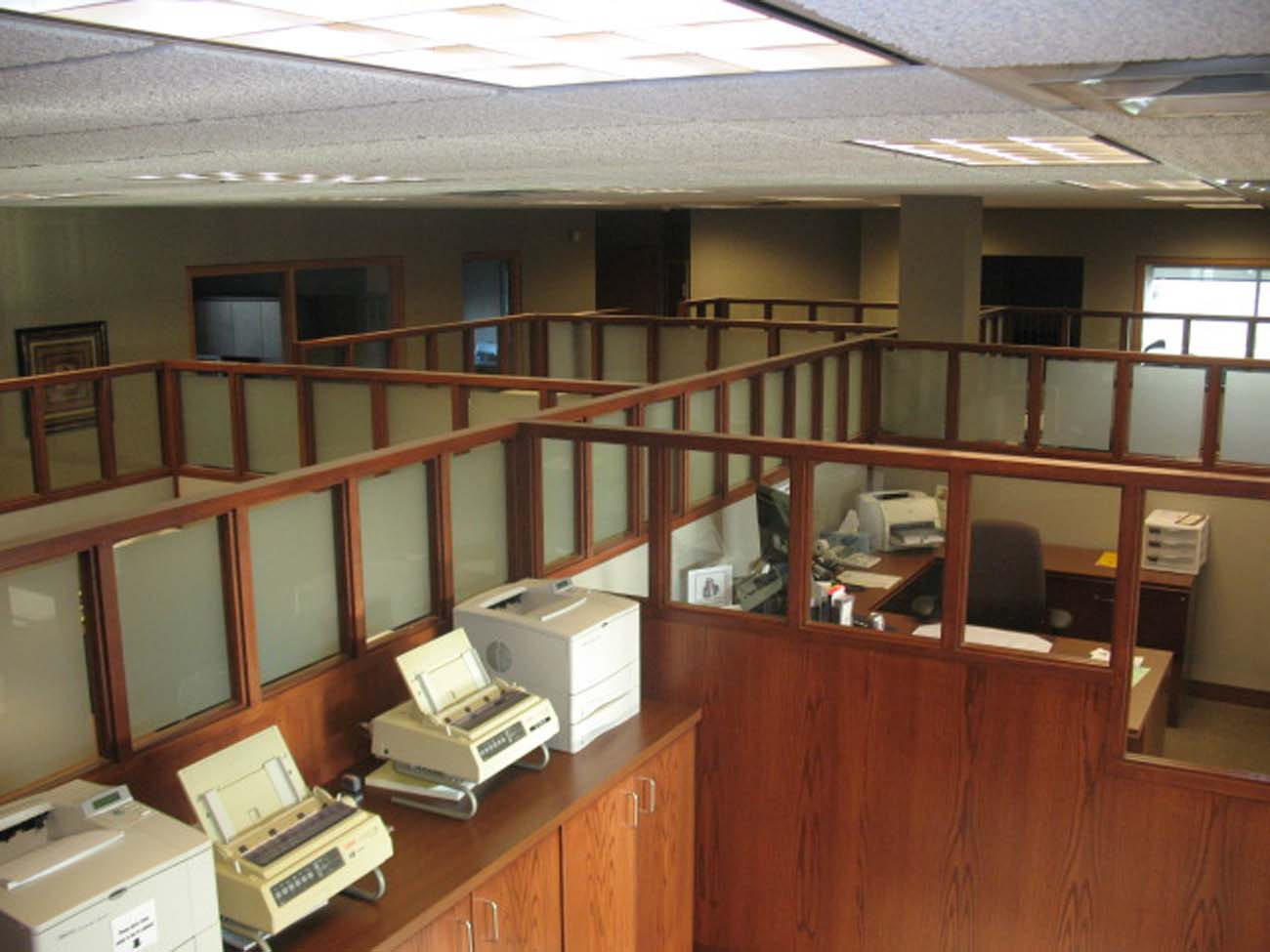 A row of cubicles in an office with printers on the counter