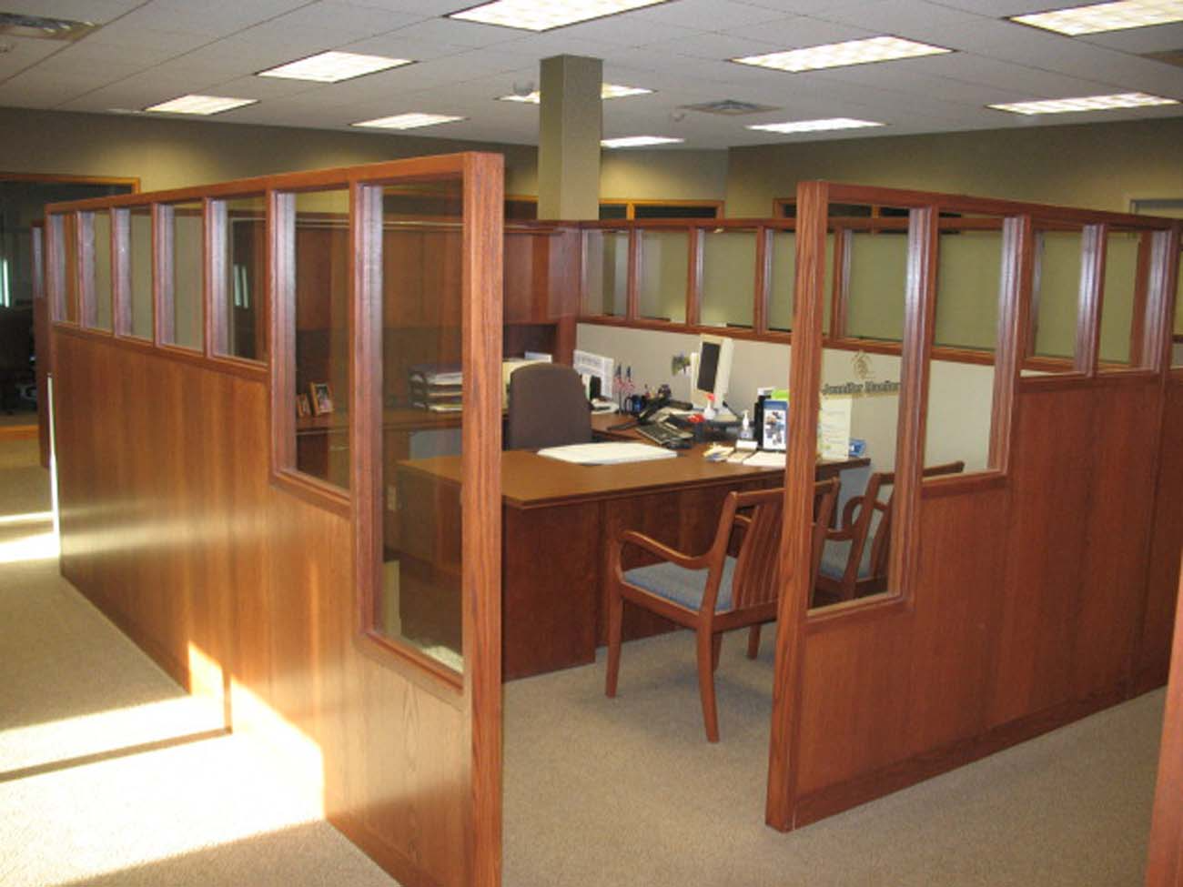 A cubicle in an office with a desk and chairs