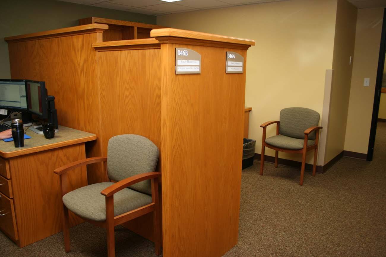 A cubicle with two chairs and a desk with a computer on it