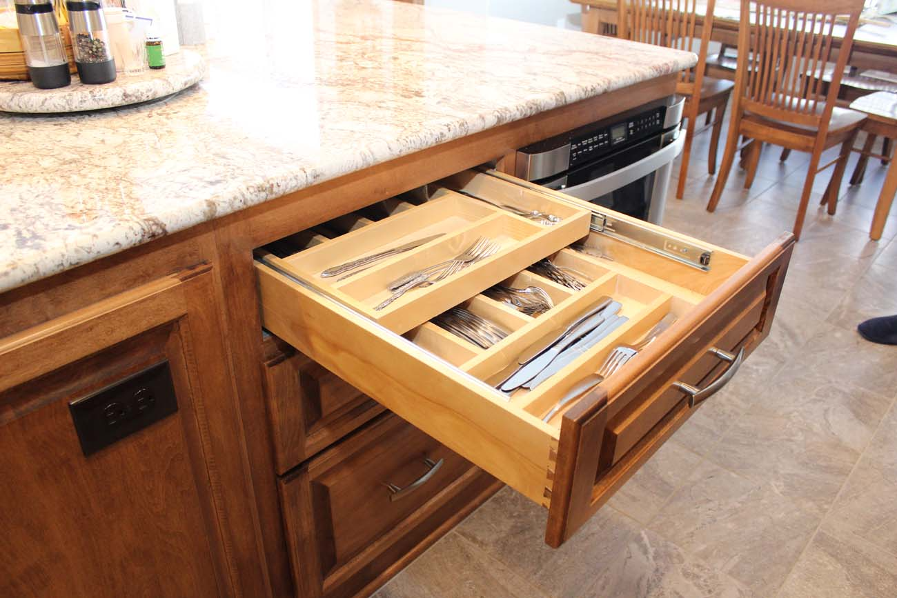 A wooden cutlery drawer is open in a kitchen.