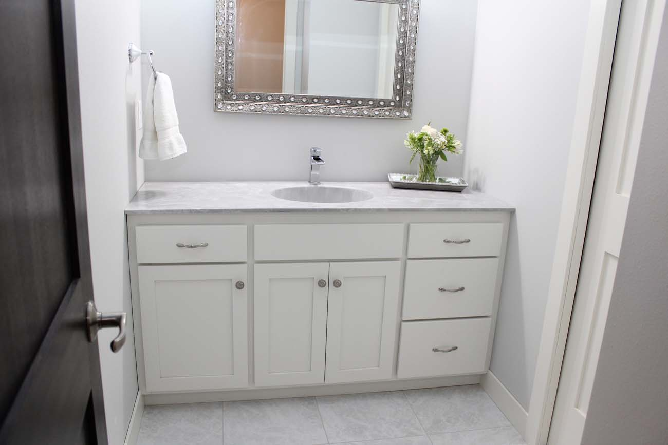 A bathroom with white cabinets , drawers , a sink and a mirror.