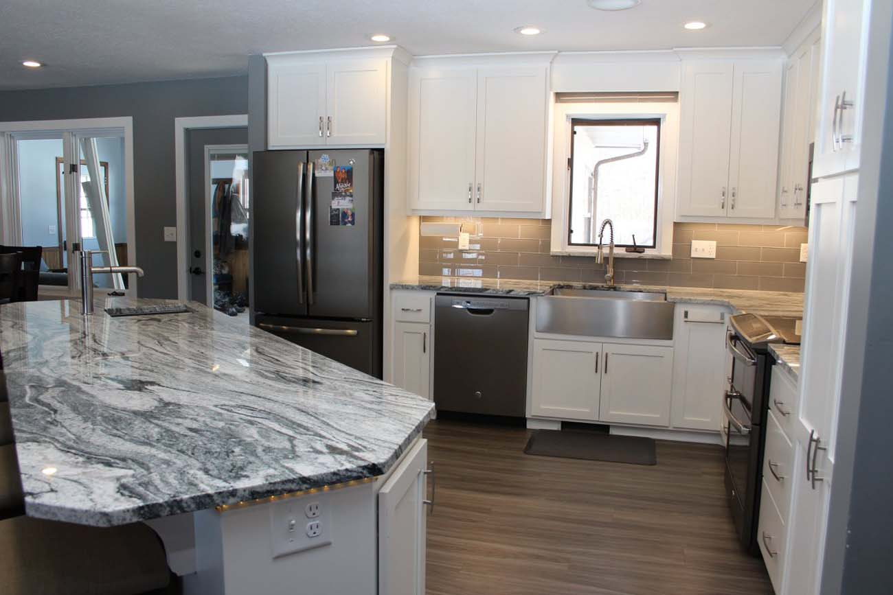 A kitchen with white cabinets , granite counter tops , stainless steel appliances and a large island.