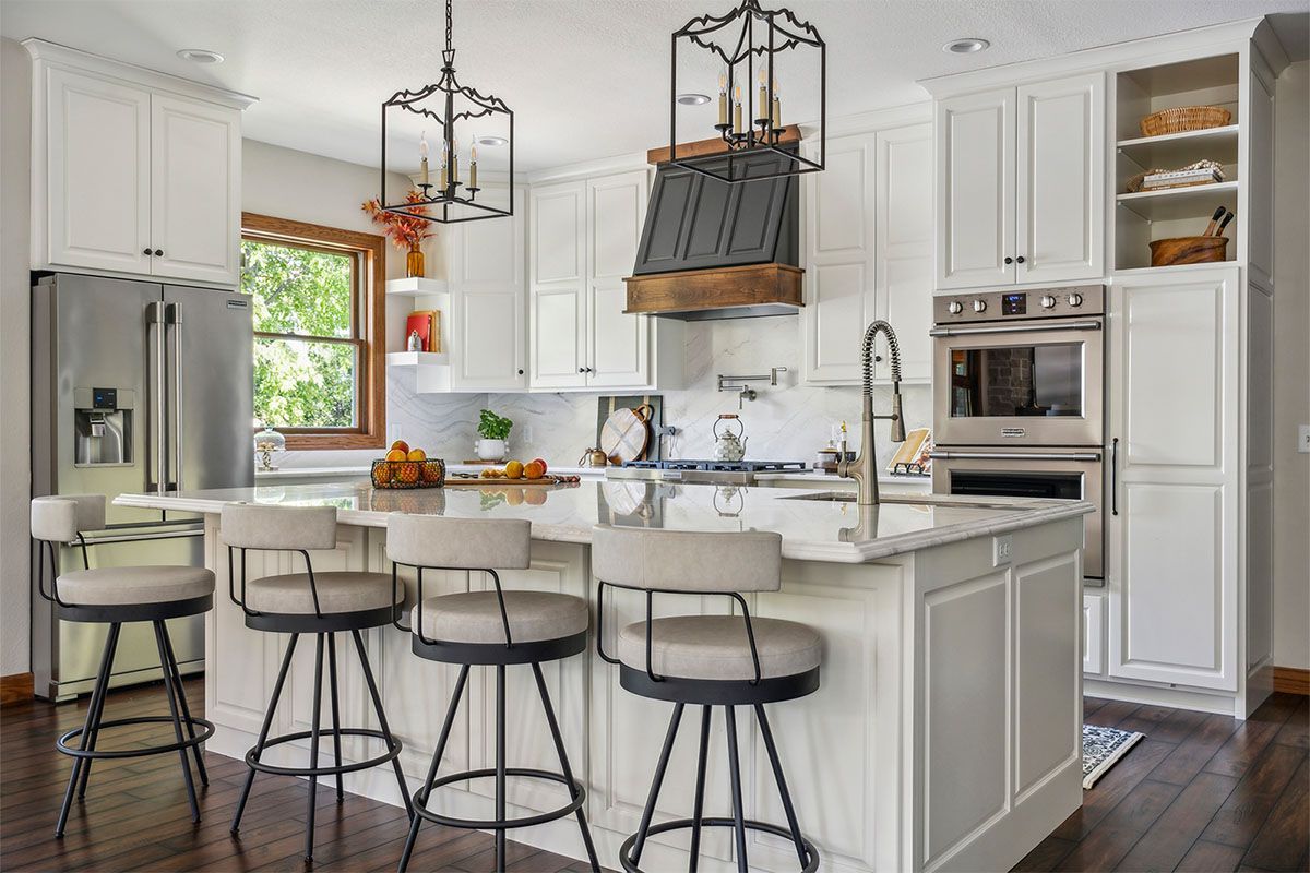 A kitchen with white cabinets and stools and a large island.