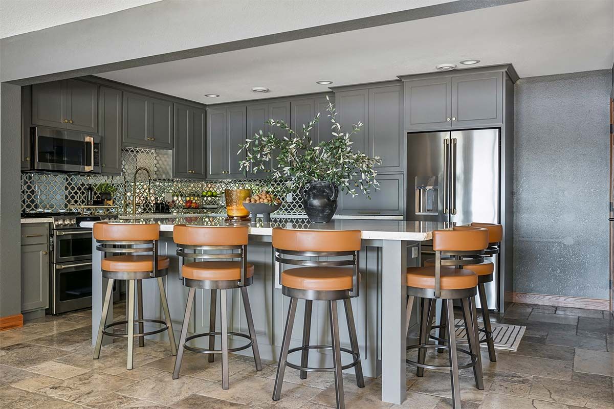 A kitchen with gray cabinets , stainless steel appliances , and a large island with stools.