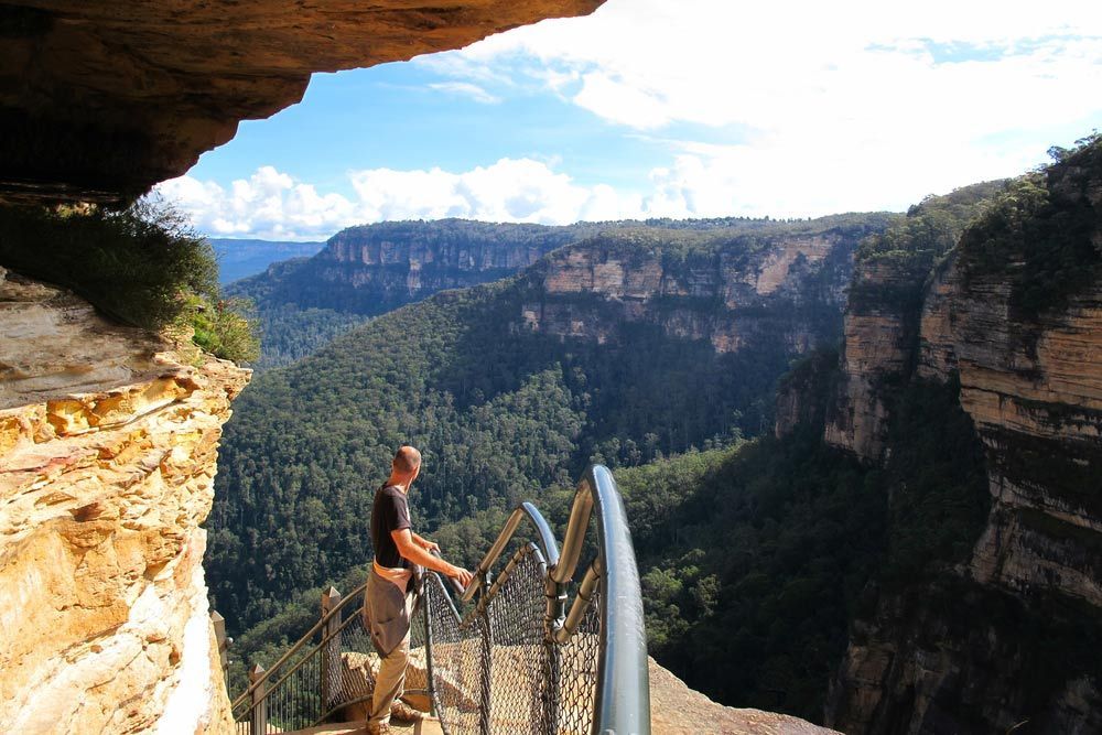 A Man Is Standing On A Cliff Overlooking A Valley — Gordy's Furniture Removals in Katoomba, NSW