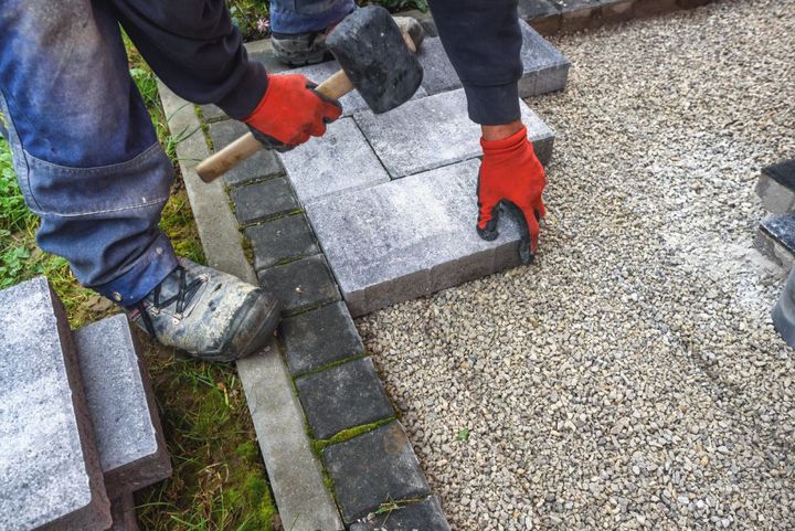 a man is using a hammer to hammer bricks on a driveway .