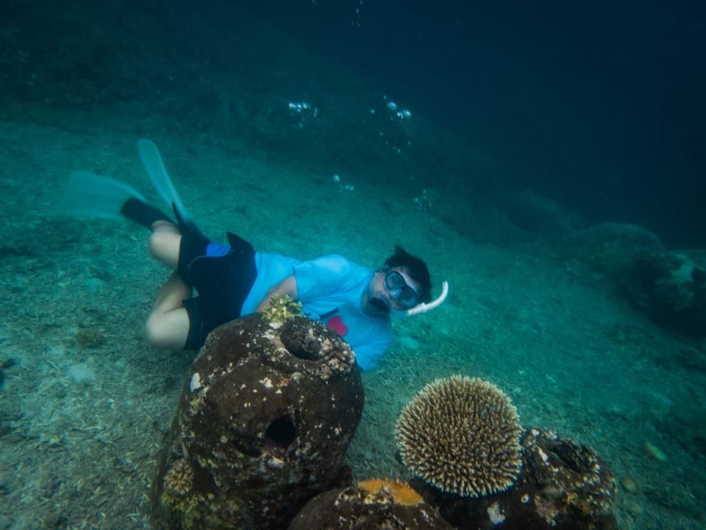 A man in a blue shirt is swimming in the ocean