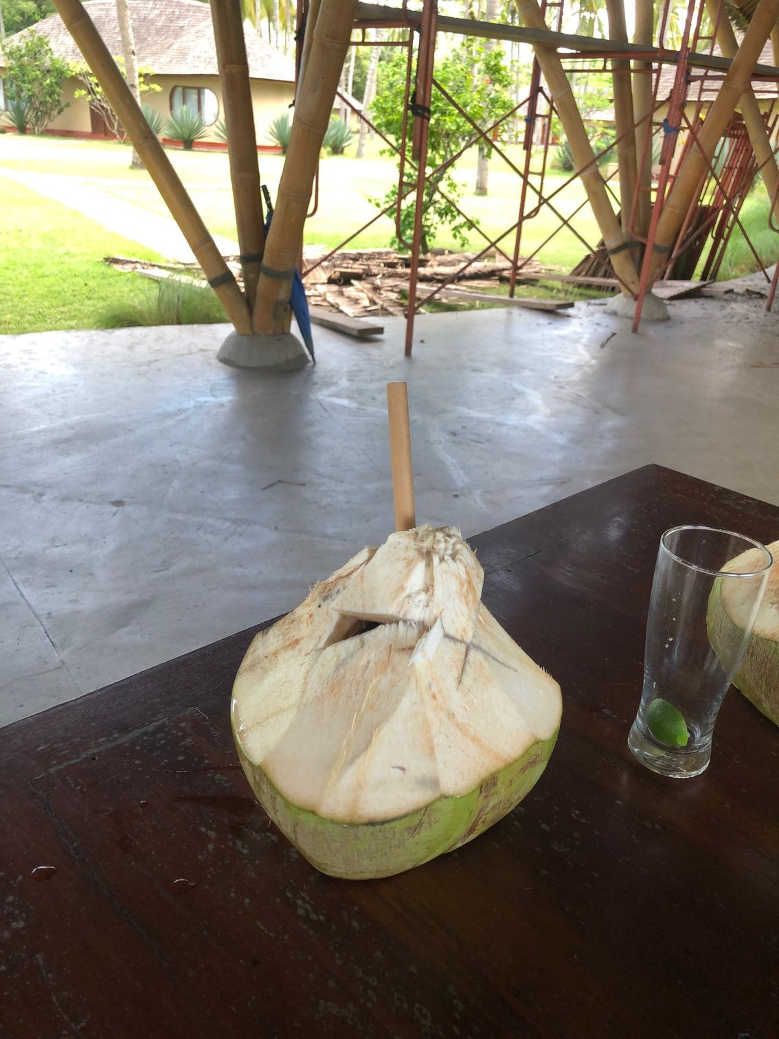 A coconut with a stick sticking out of it sits on a table next to a glass